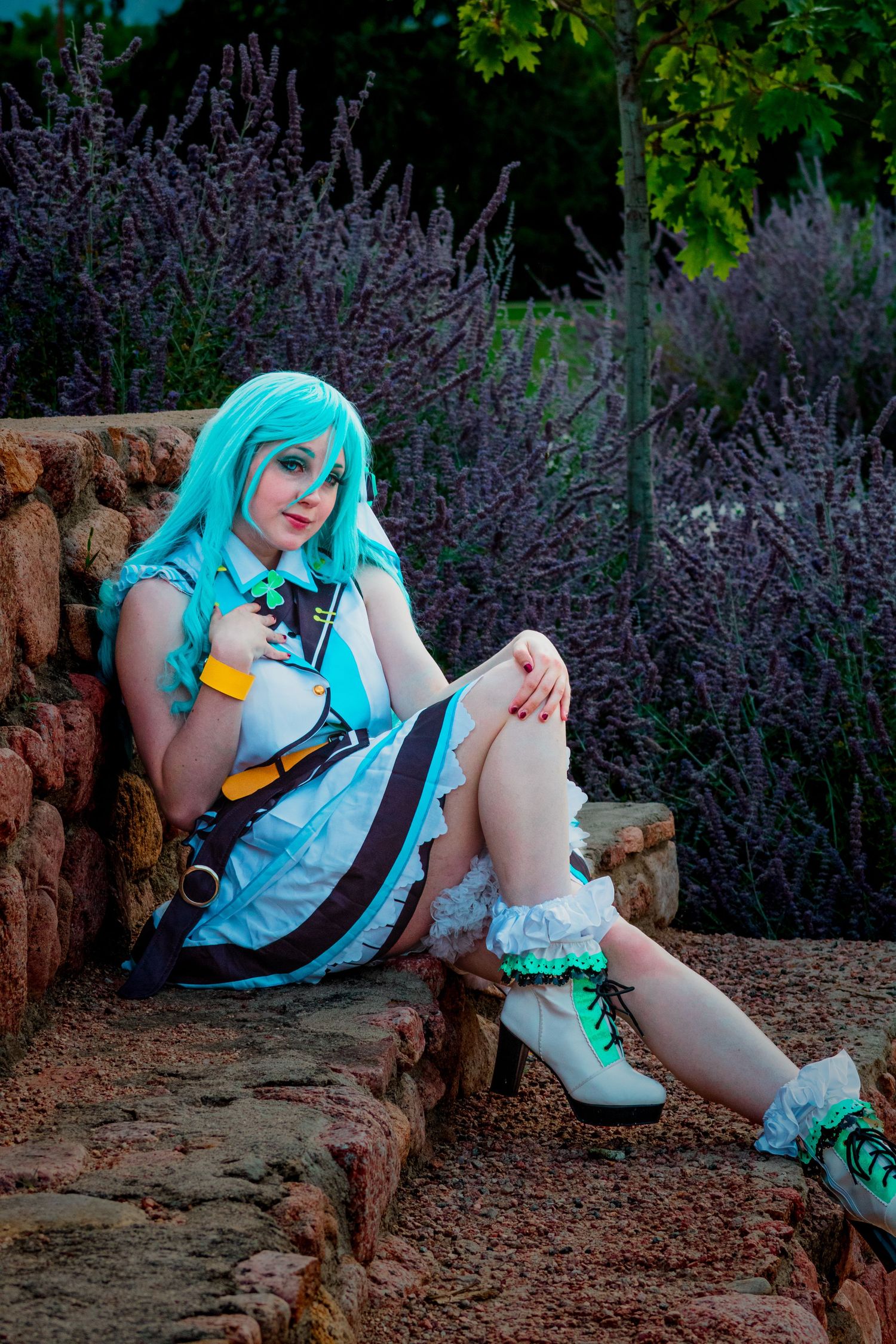 Cosplay scene with turquoise wig and dress outfit sitting on stone steps near blooming purple lavender flowers.