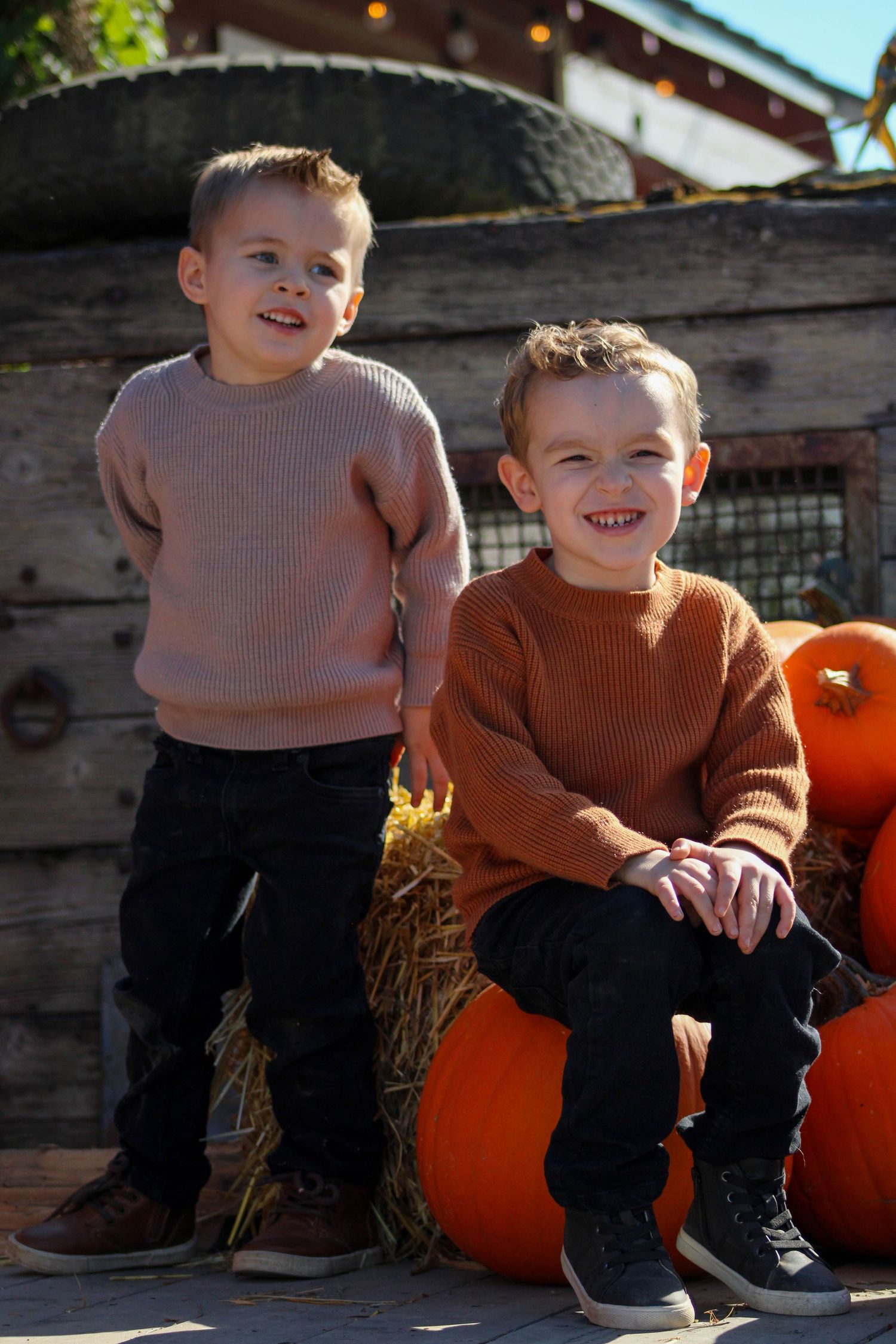 Children in matching sweaters smile while sitting on pumpkins during fall.