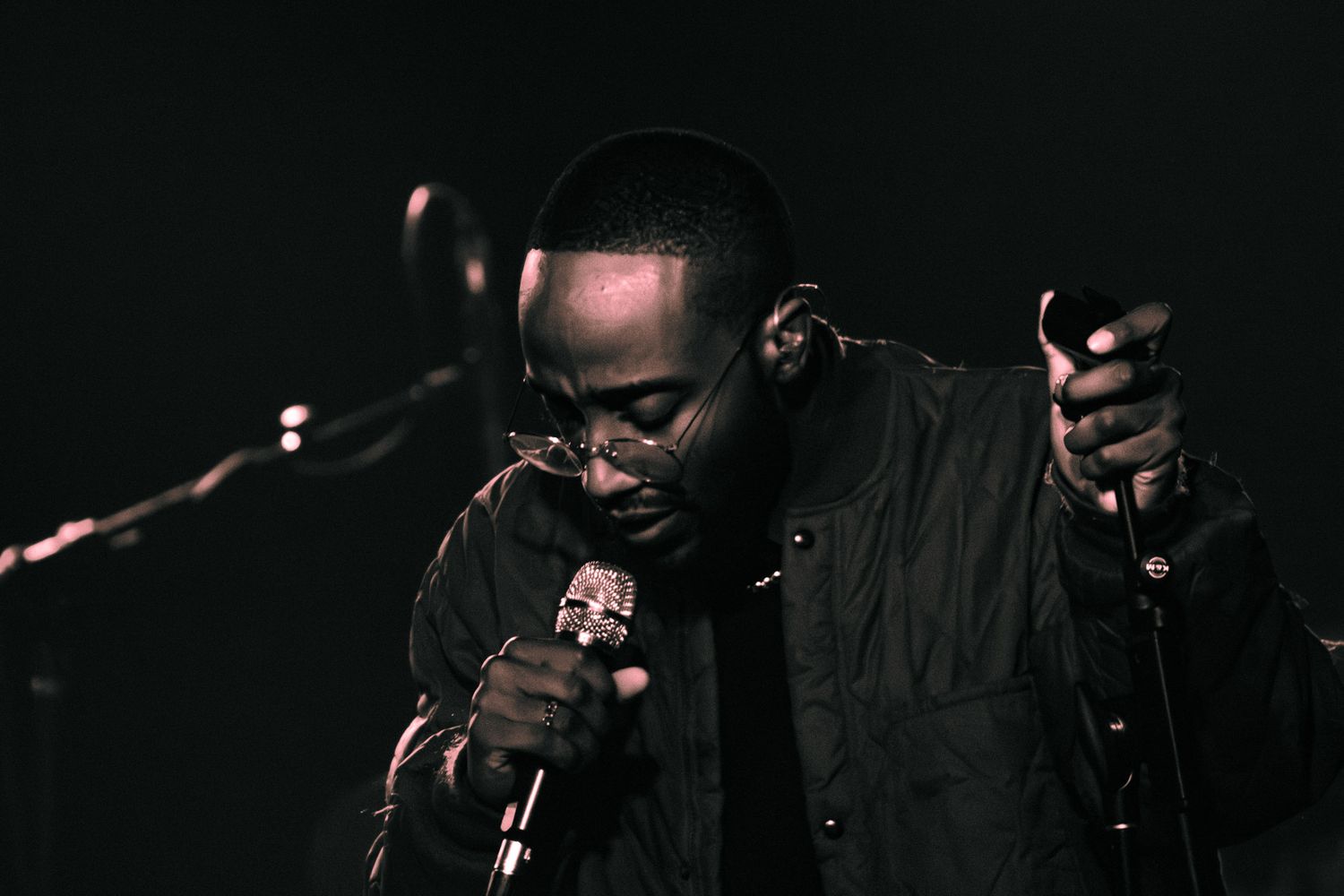 Black and white photo of a male vocalist performing on stage, leaning into a microphone with intensity.