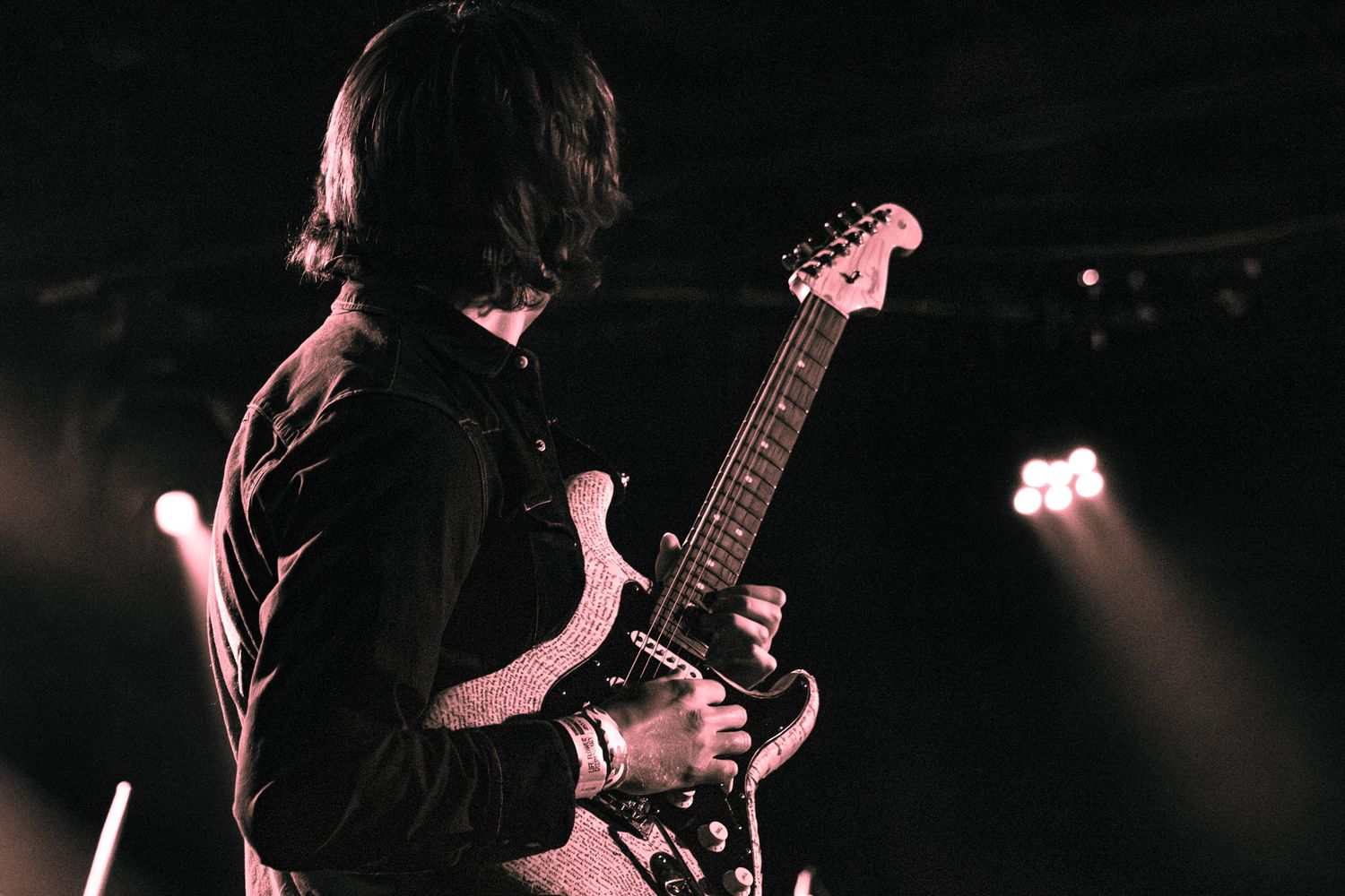 Guitarist performing on stage with dramatic lighting, playing electric guitar at a live music concert.