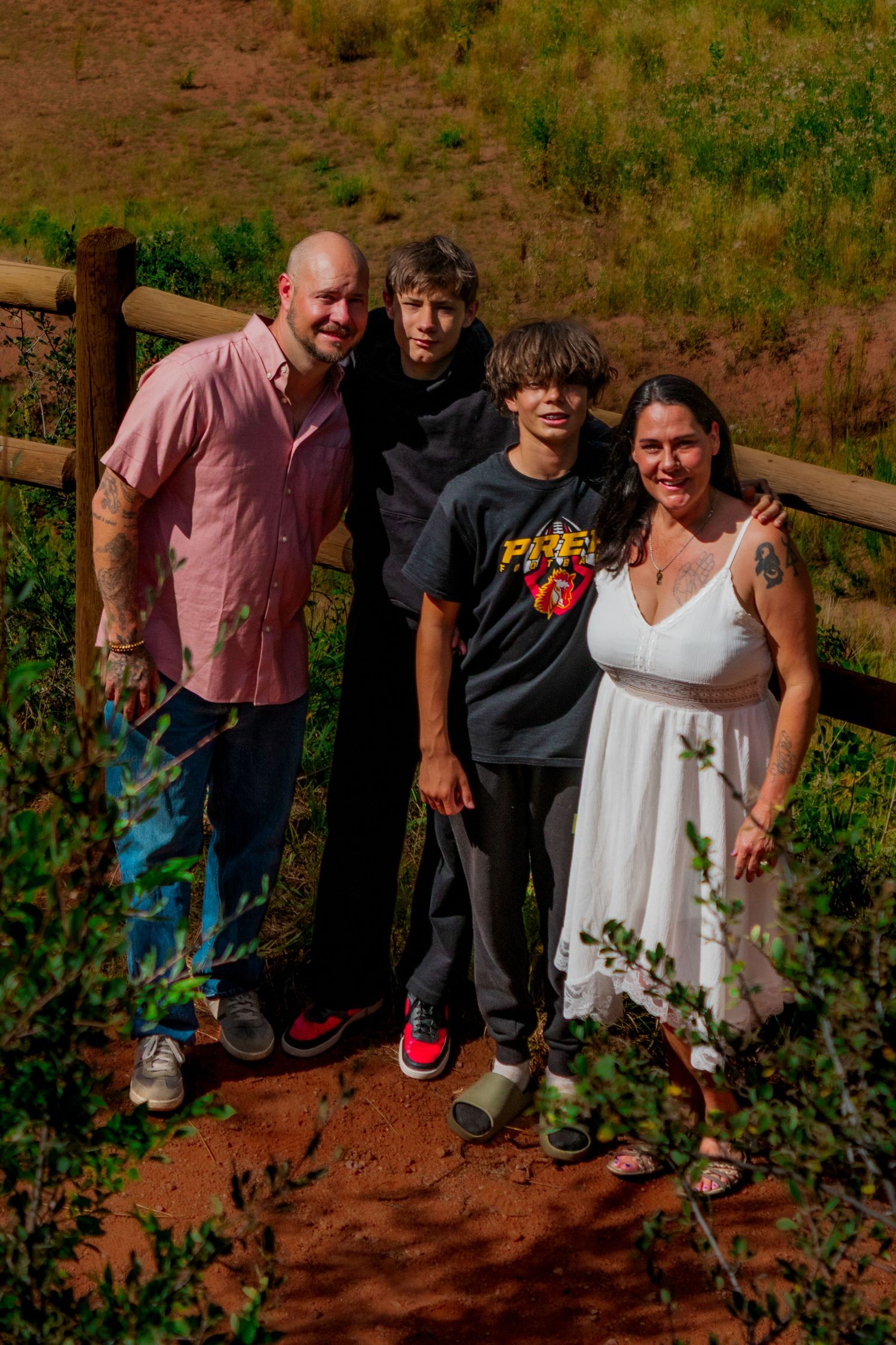 A family stands together on a dirt hiking trail surrounded by greenery on a sunny day.