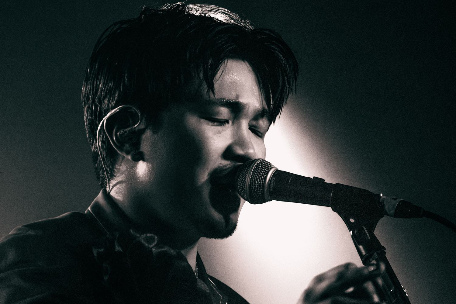 Young male vocalist performing live on stage, singing passionately into a microphone in black and white lighting.