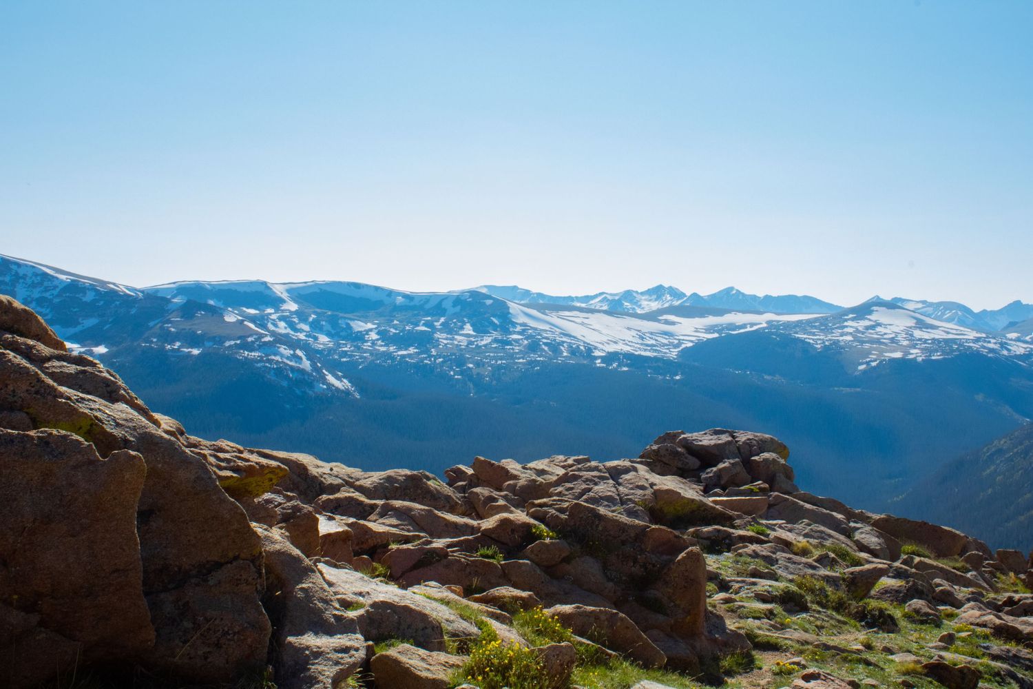 Rocky mountain vista with snow patches and rugged terrain extending to distant peaks under clear skies.