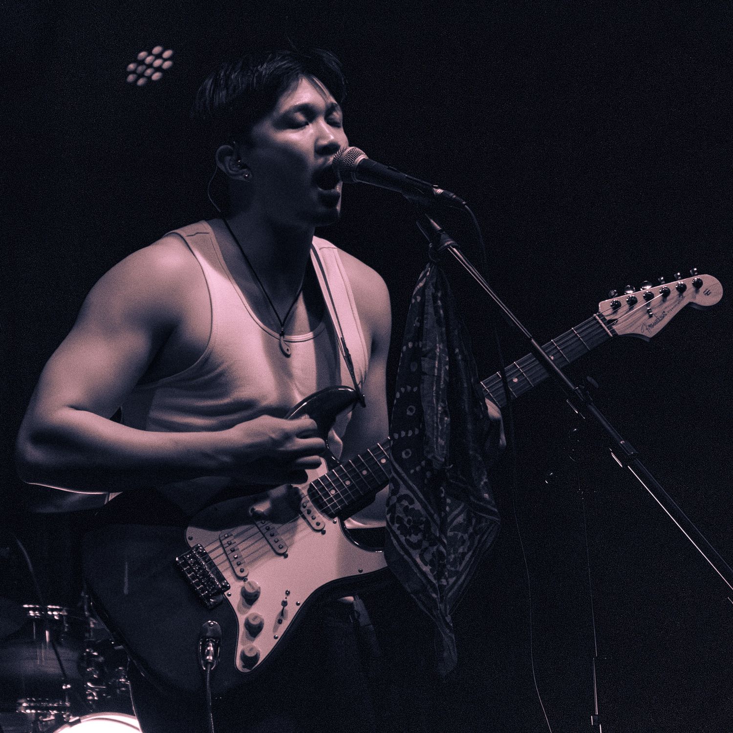 Musician playing electric guitar and singing into microphone on stage in black and white.
