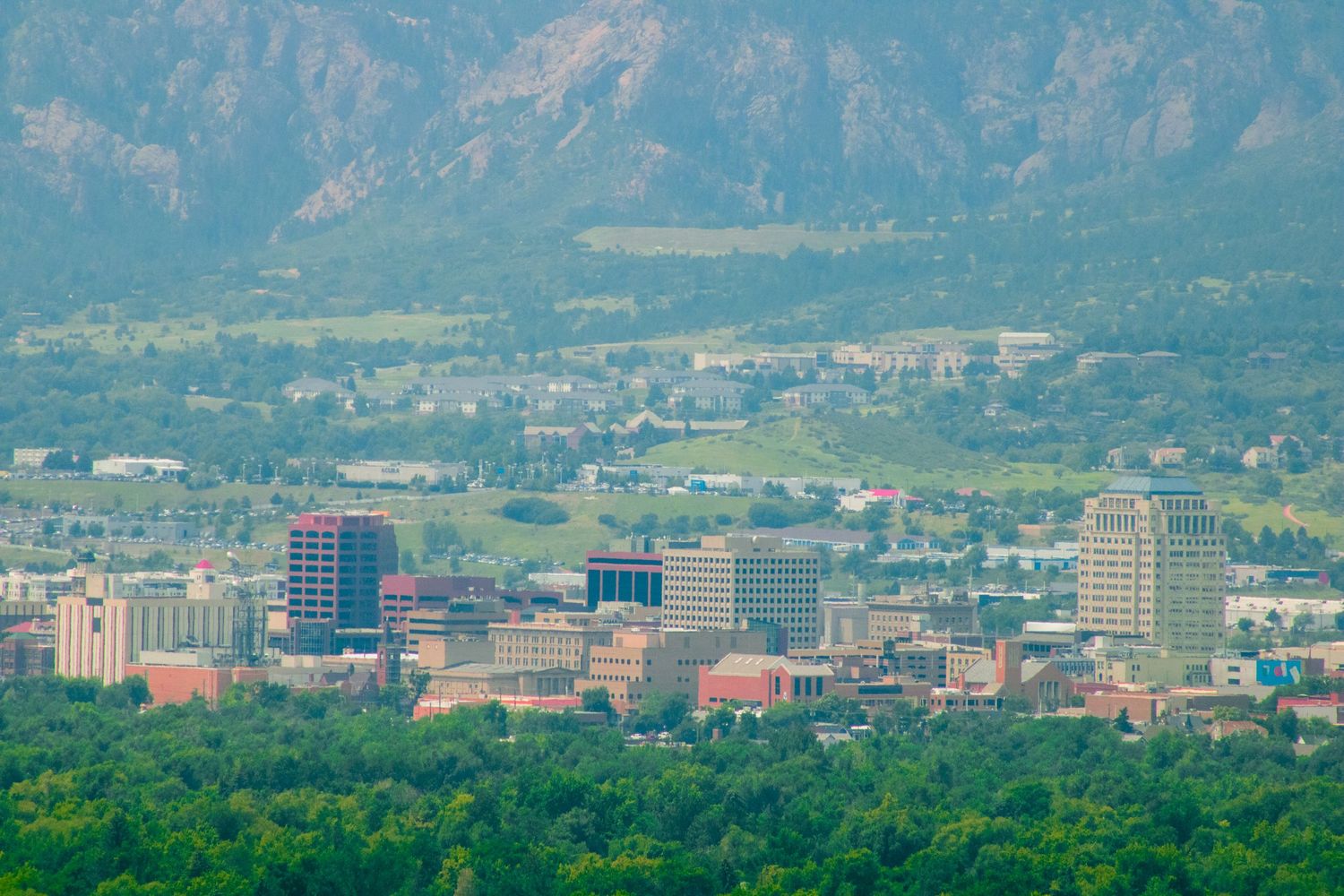 Downtown Colorado Springs skyline with towering office buildings backed by dramatic mountain peaks.