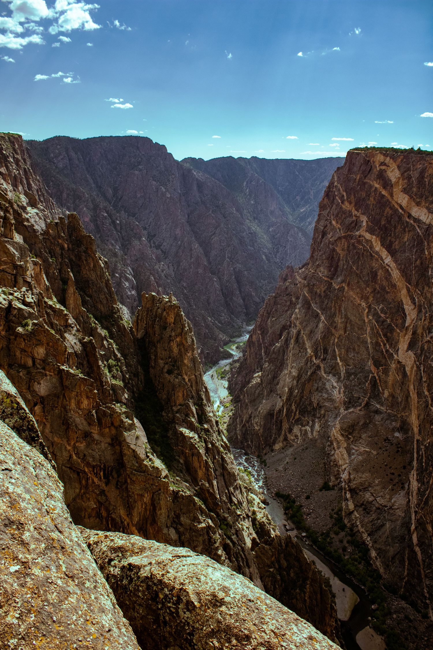 Dramatic rugged canyon walls with steep cliffs and a winding river visible far below under bright blue skies.