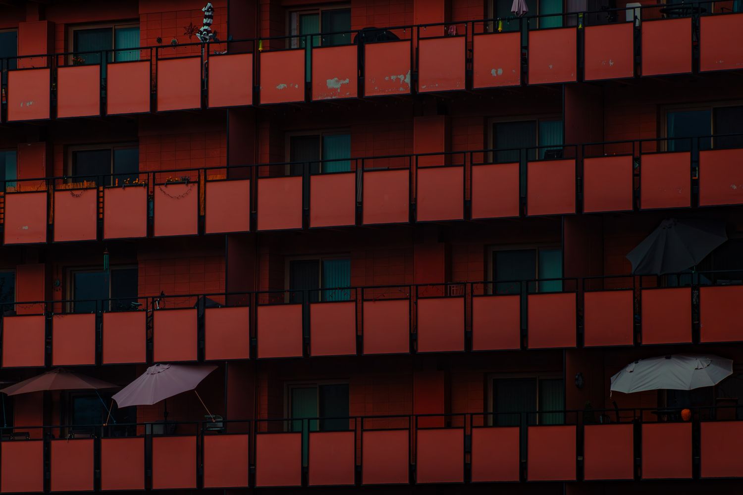 A brutalist building facade with red-orange panels and dark windows creating a geometric pattern in low light.