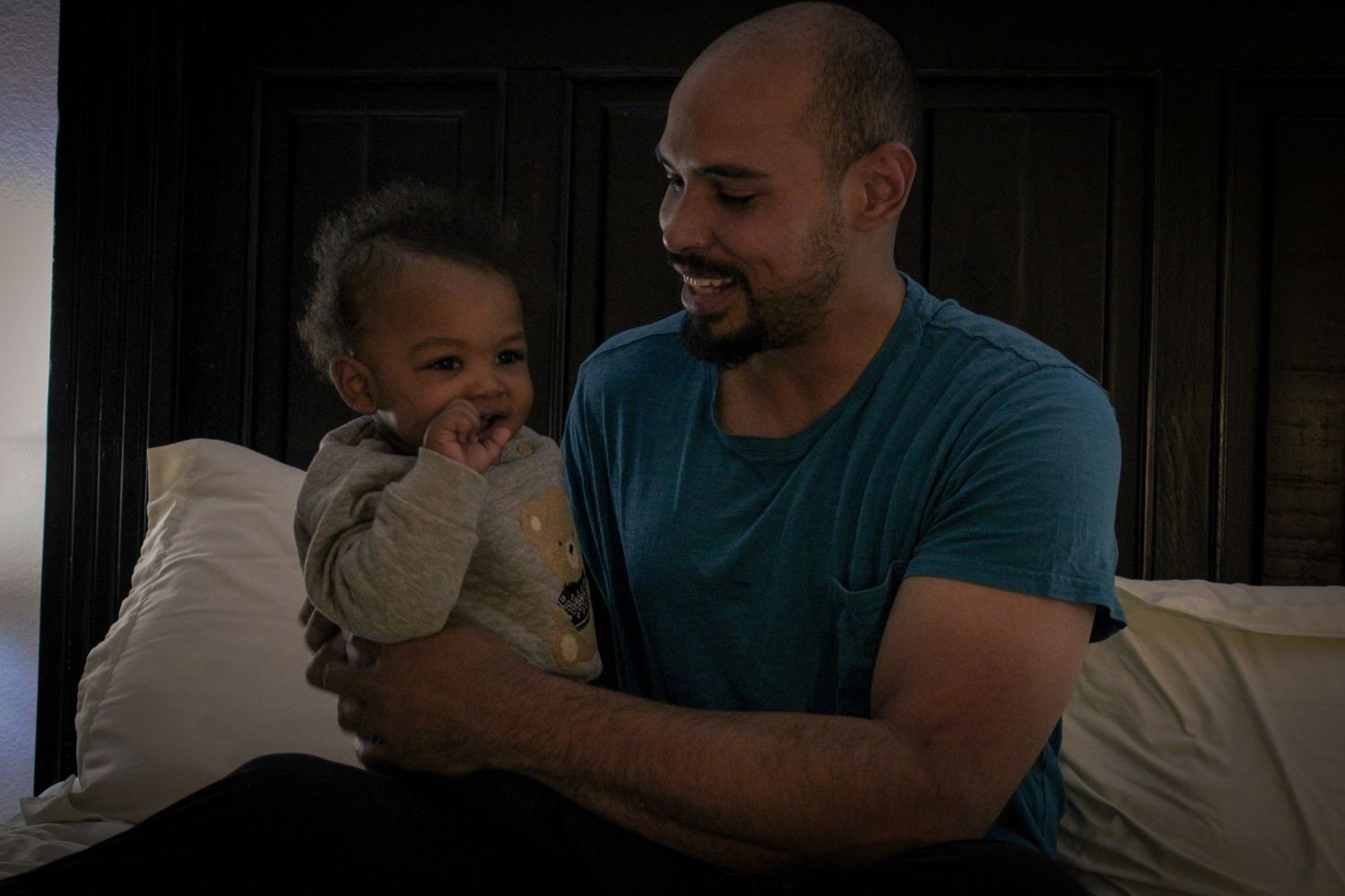 People resting together in a dimly lit bedroom with dark wooden furniture.