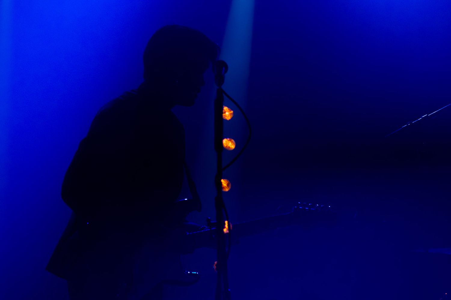 Silhouetted musician performing on stage bathed in dramatic blue light with warm stage lights glowing in the background.