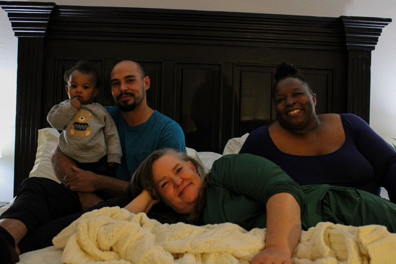 People relaxing together on a large white bed in a dimly lit room.