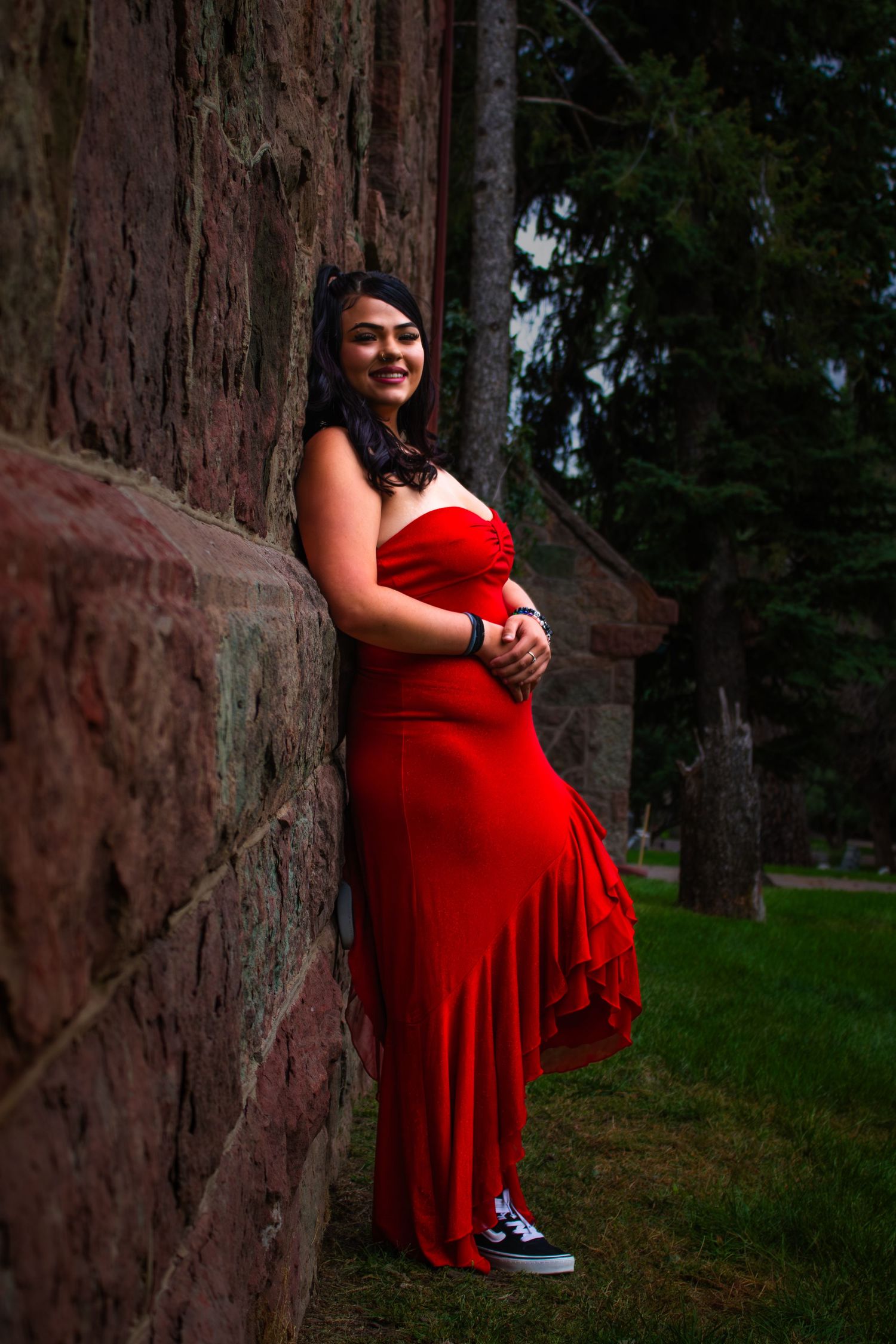 A maternity photo series in a wooded setting shows someone in a flowing red dress posing against tall tree trunks.