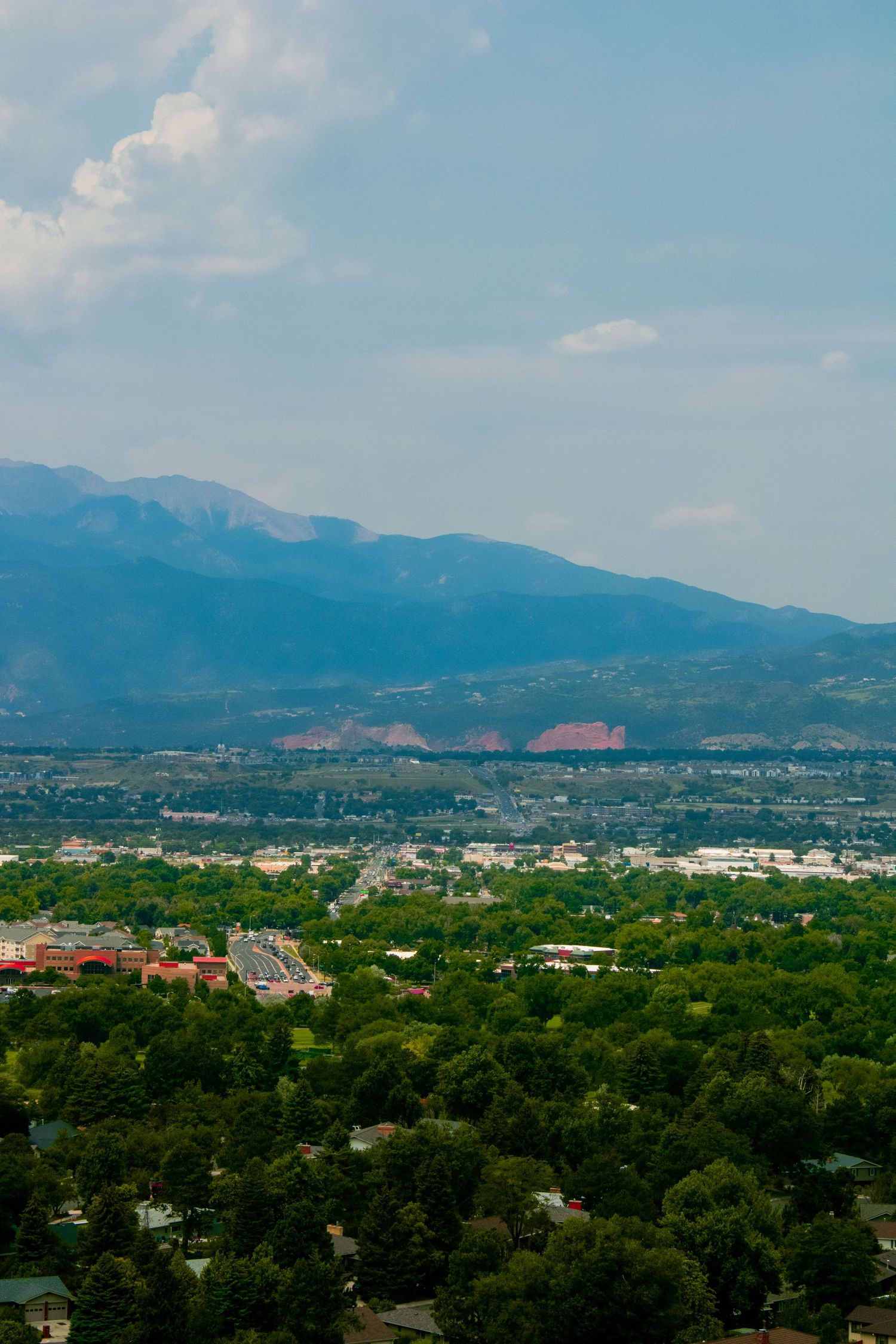 Scenic overlook of Colorado Springs showing lush forest, city buildings and majestic mountain backdrop.