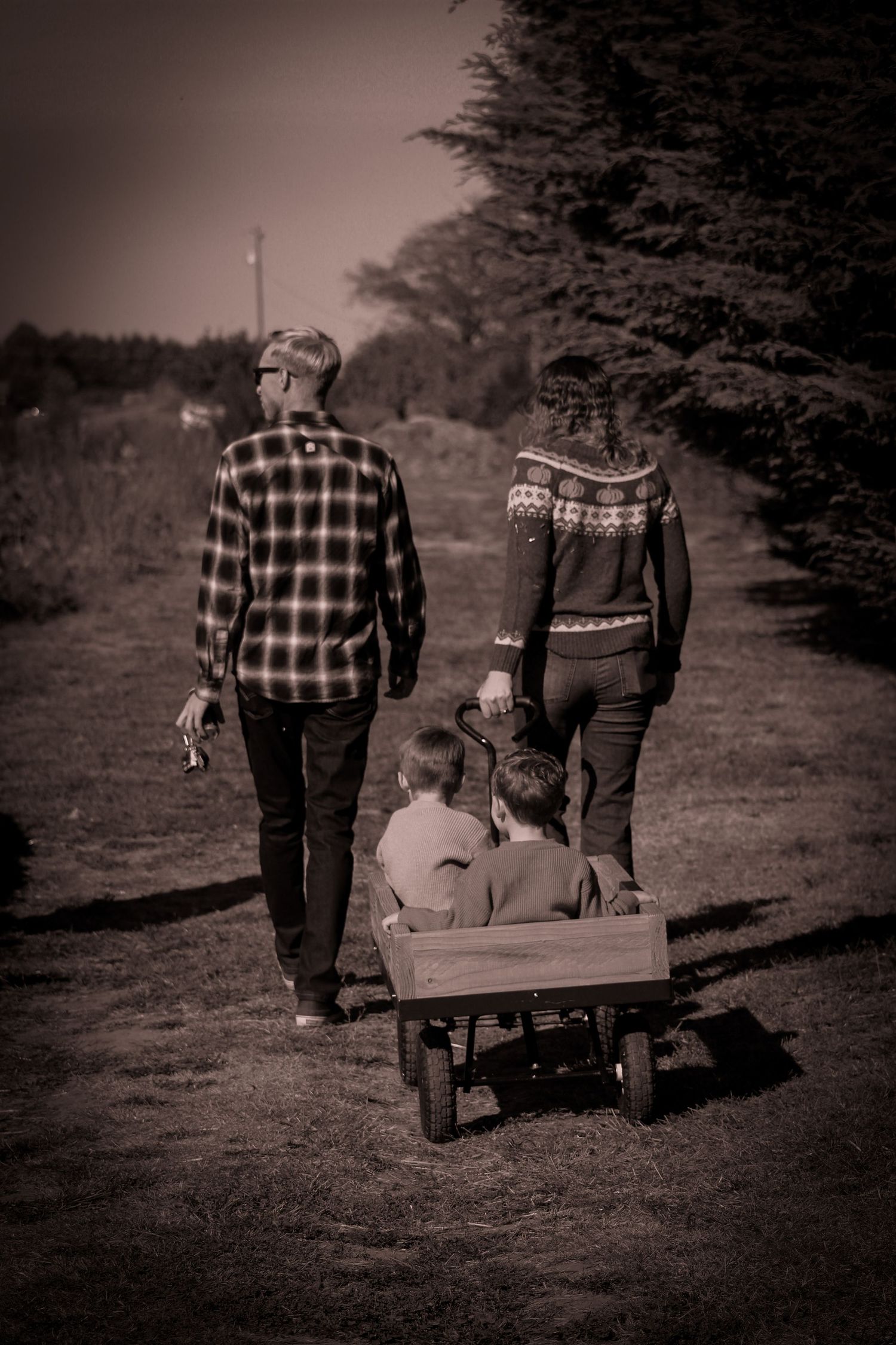 Vintage-style black and white photo of people walking with a wagon through meadow.