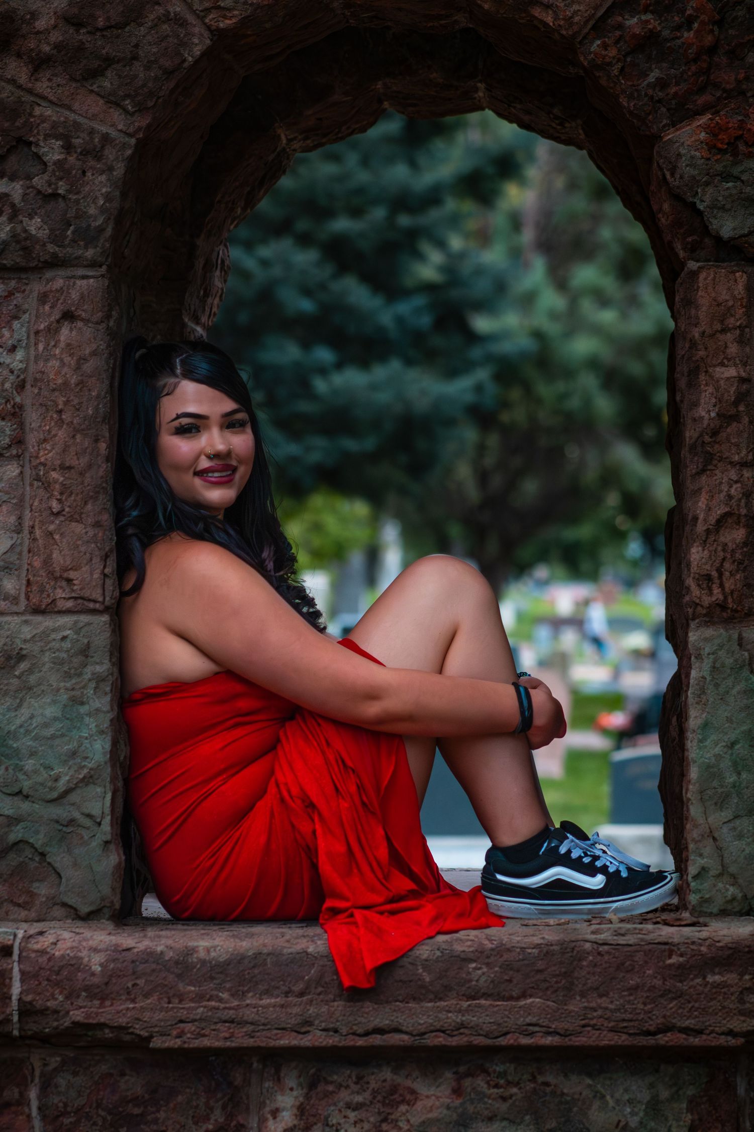 Five artistic photos show someone in a vibrant red dress reclining against stone archways in an outdoor setting.