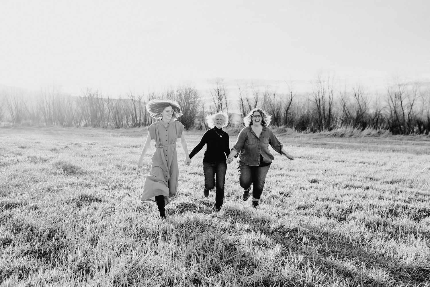 Three people running and holding hands together in a field on a misty morning, captured in black and white.