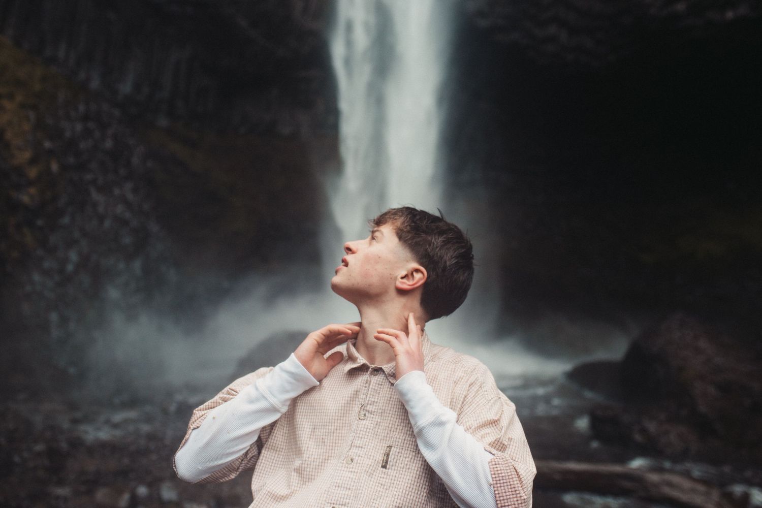 A person standing near a majestic waterfall amidst misty scenery.