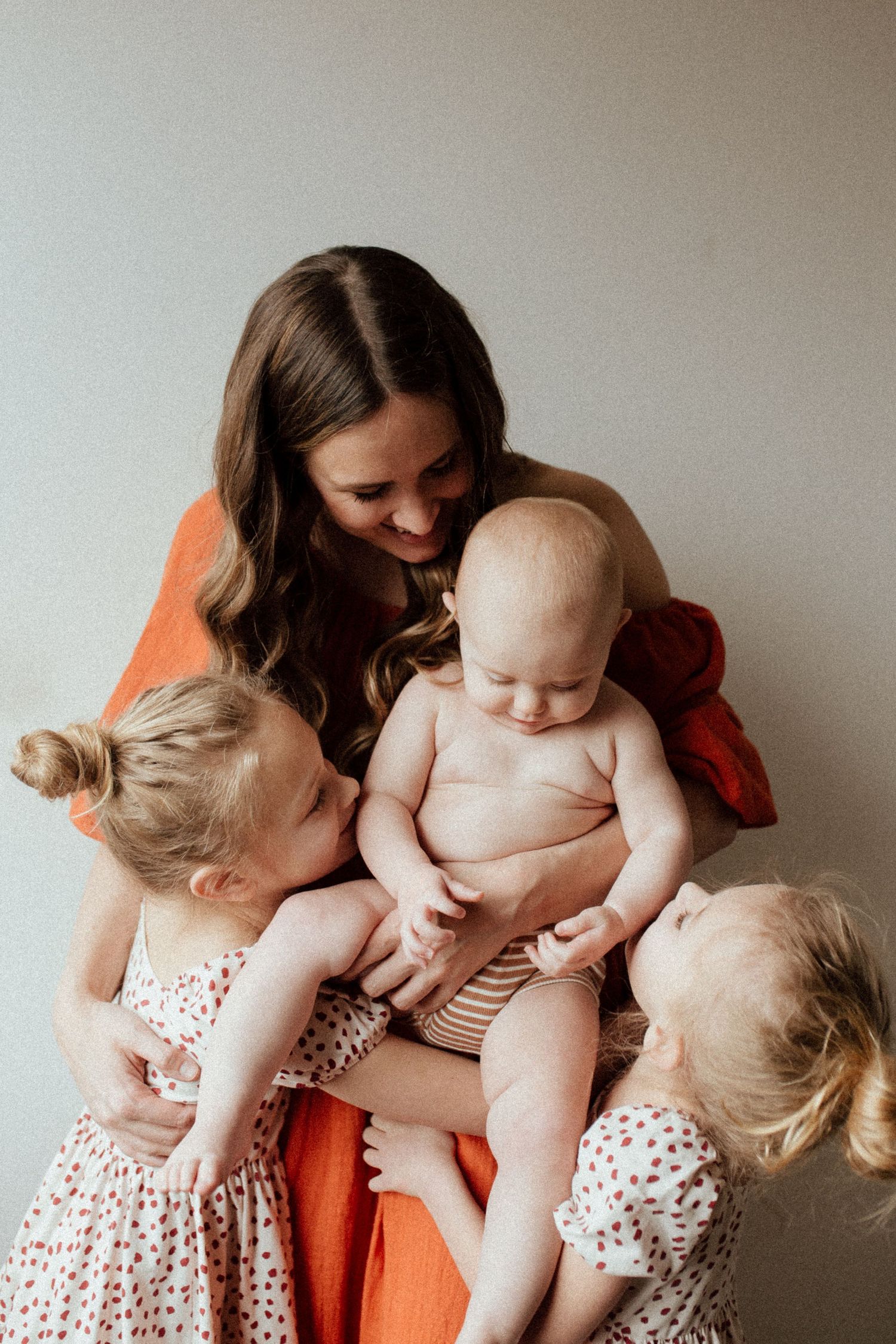 A series of tender moments between a mother in an orange dress and her two children in red and white polka dot dresses.