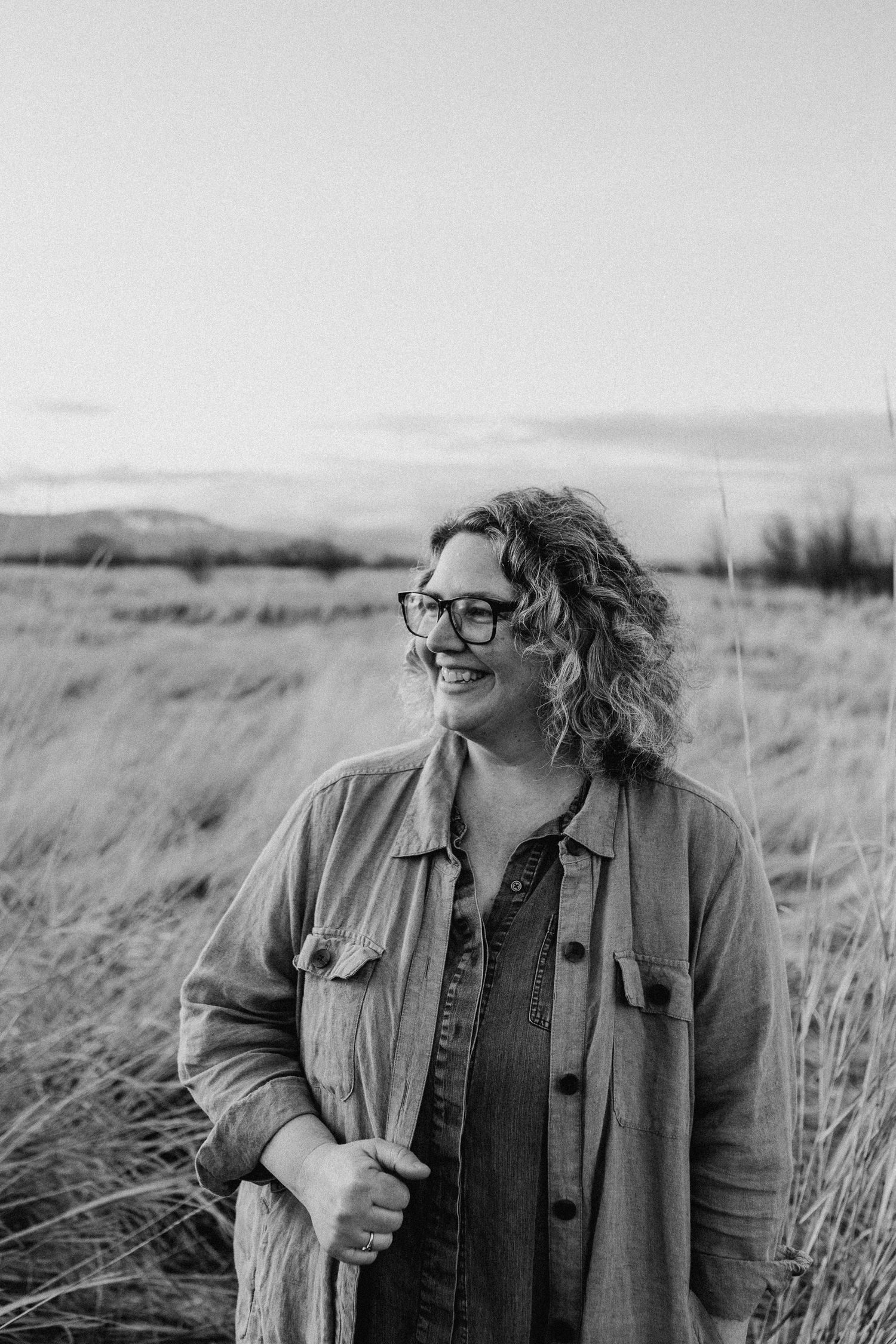 Black and white portrait in a windswept field with grass and hills in the background.