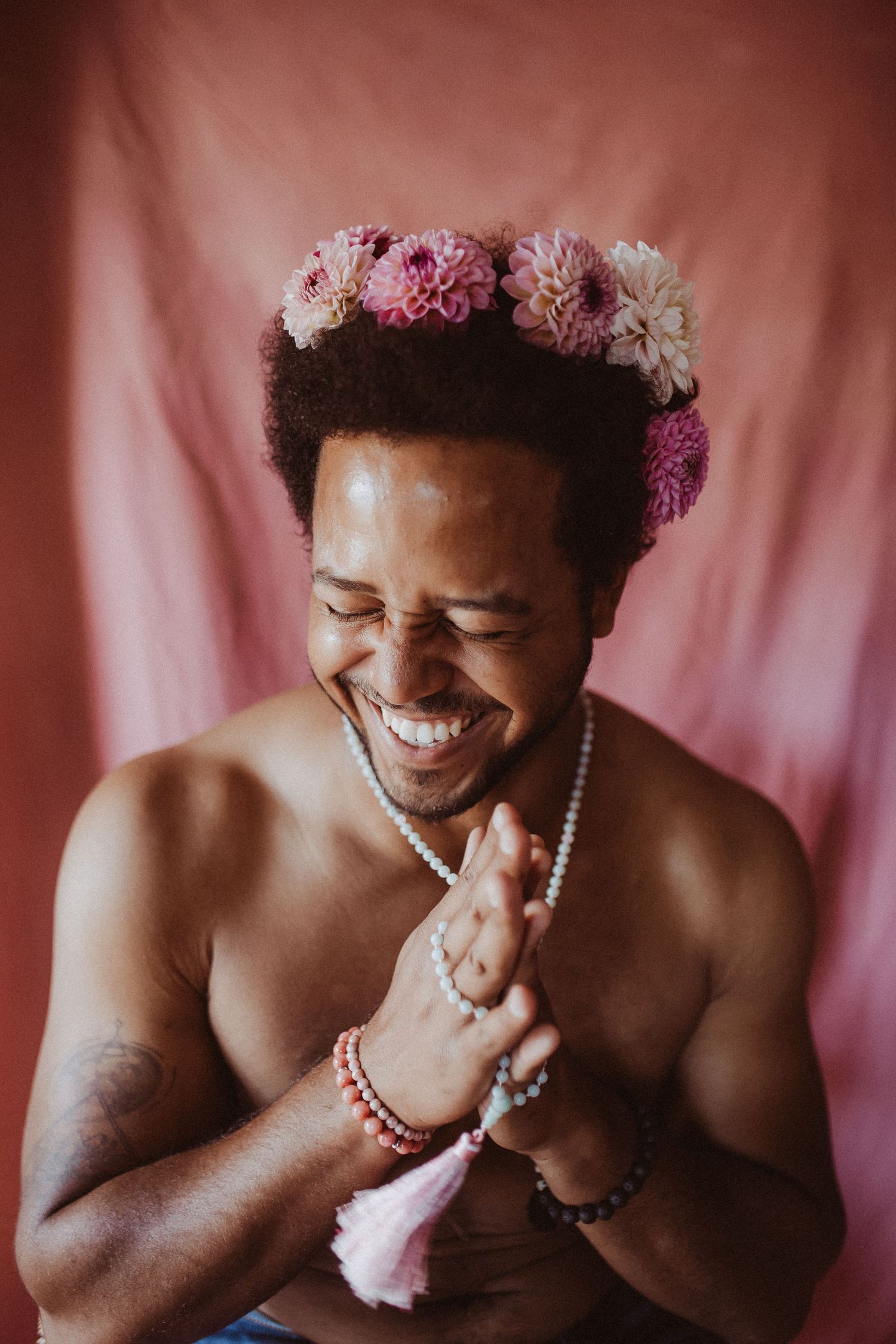Person wearing a flower crown laughs joyfully against a pink backdrop in a series of candid expressions.