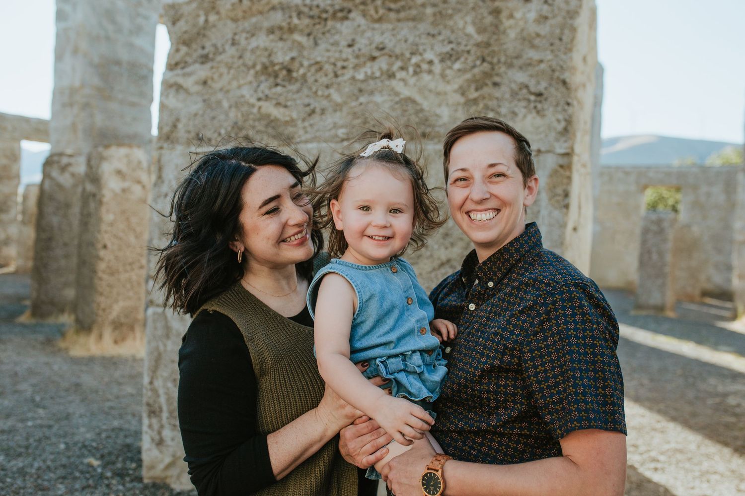A family shares joyful moments and embraces while posing outdoors against stone walls and mountain views.