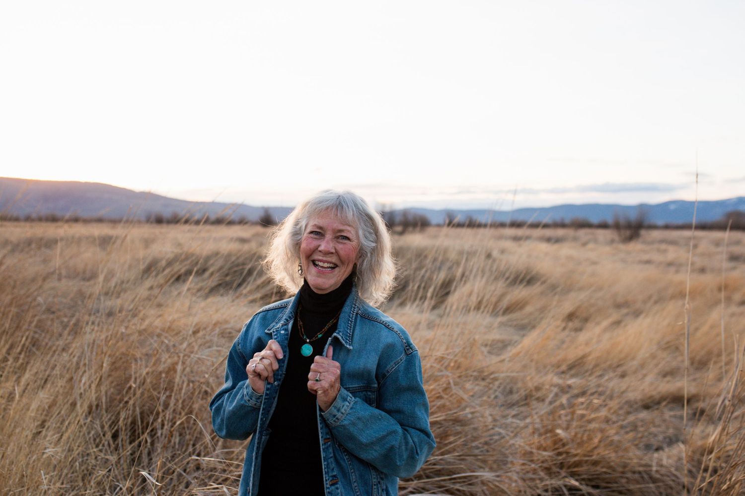 Person wearing blue coat stands cheerfully in golden grassland landscape during autumn season.