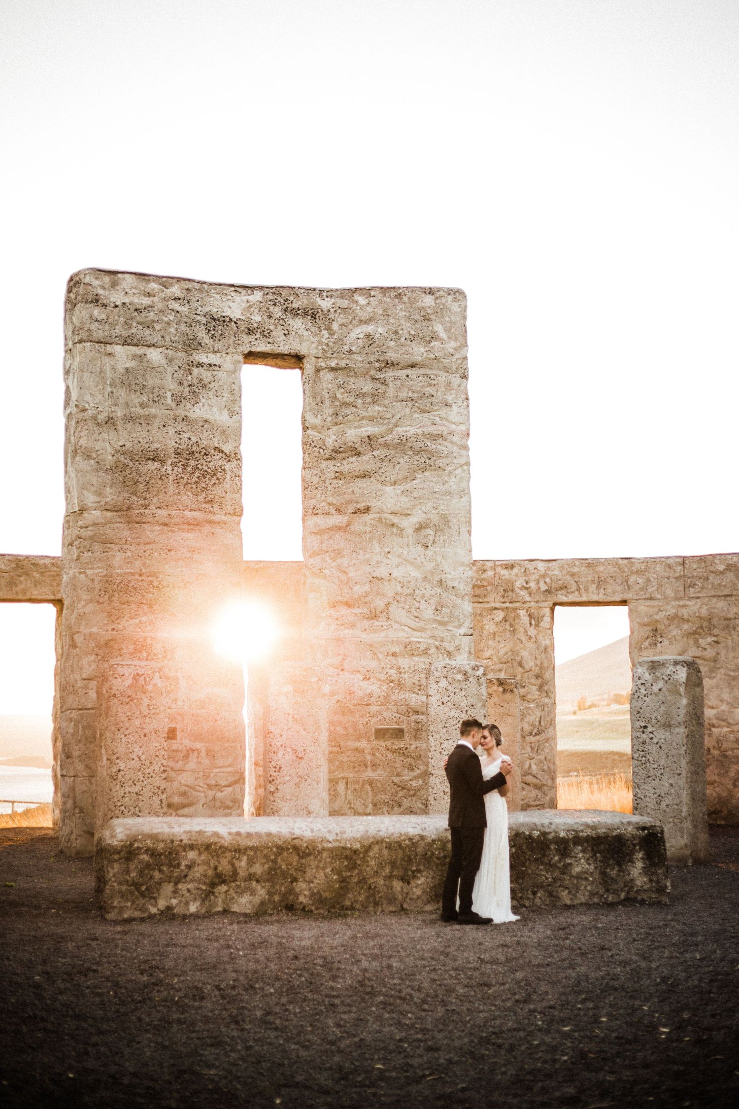 Silhouettes stand within a rustic stone structure's openings as golden sunlight streams through at sunset.