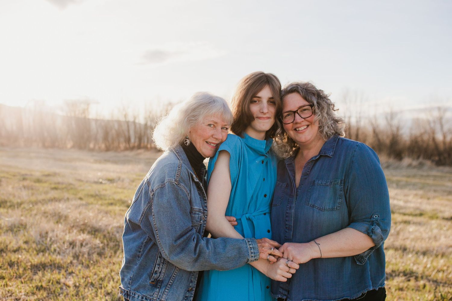Family embracing outdoors in a golden field during sunset wearing coordinating blue and gray outfits.