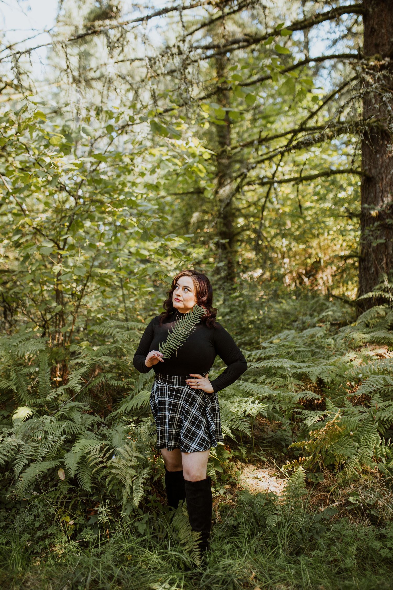 Forest scene with plaid skirt and dark sweater outfit styled with knee high socks in a moody natural setting.