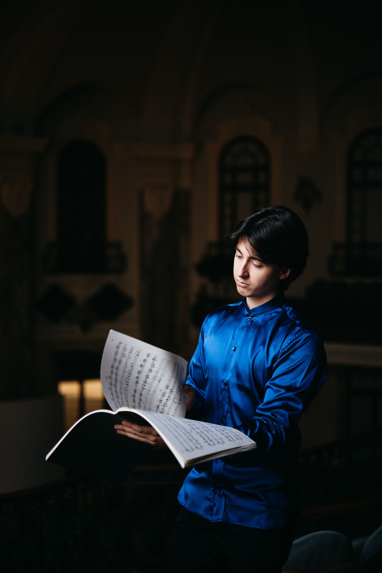 Young man in blue shirt reading sheet music in dimly lit church setting.