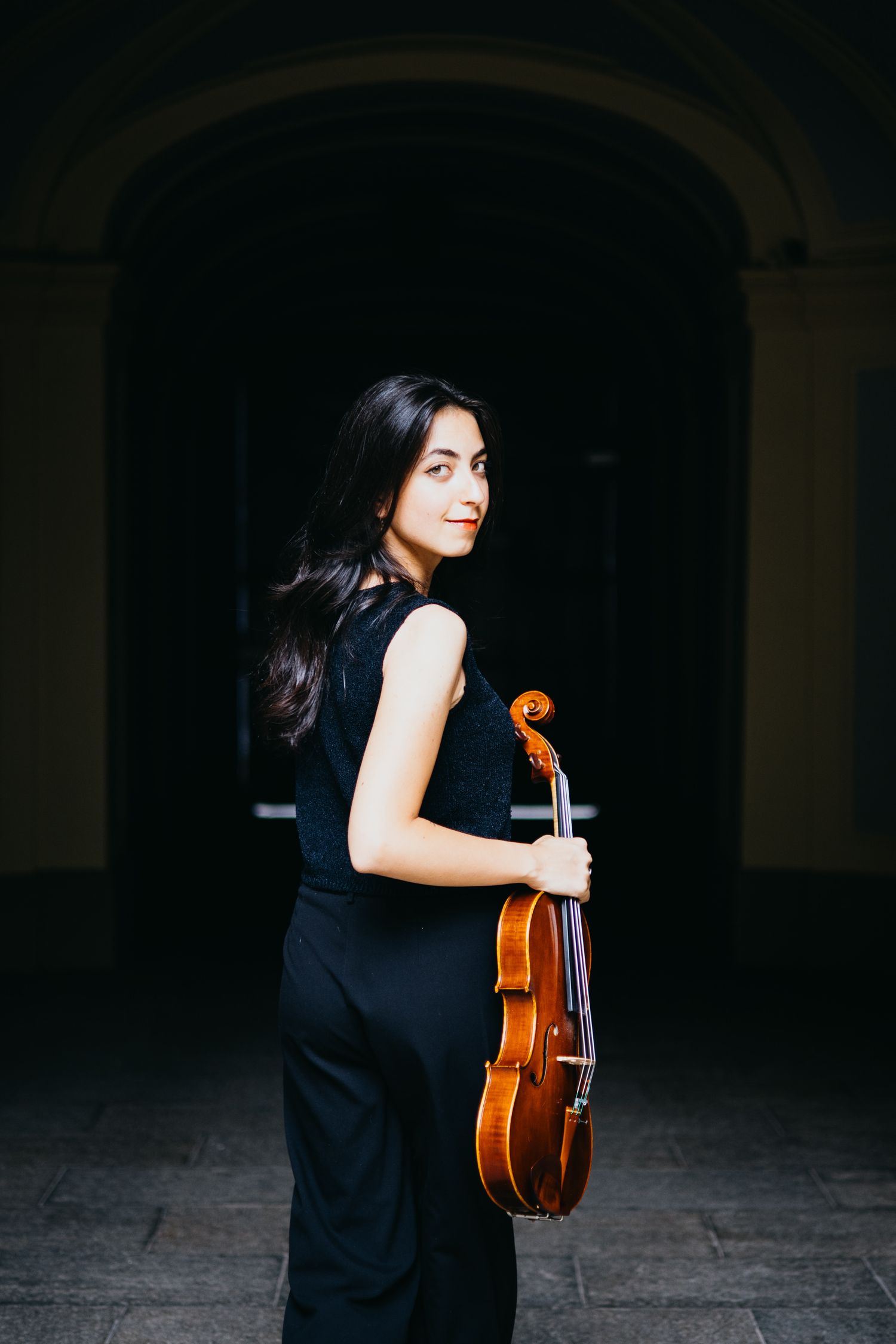 Giovane violista donna con in mano la sua viola che cammina in un corridoio con archi
