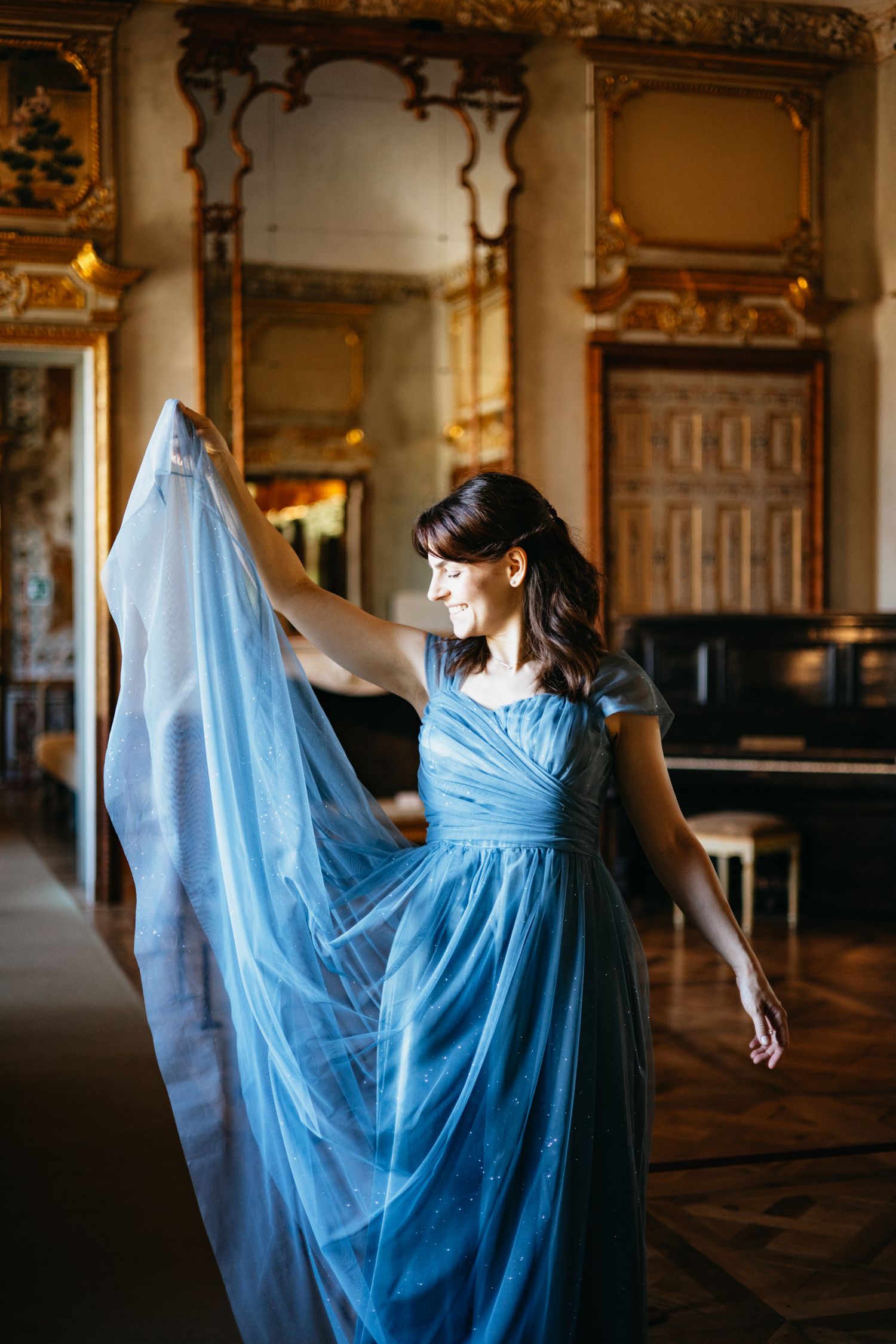 Woman in flowing blue tulle gown twirling gracefully in an ornate golden room.