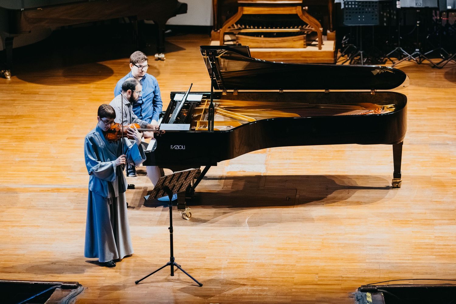 Aerial view of violinist and pianist performing on concert hall stage with grand piano.