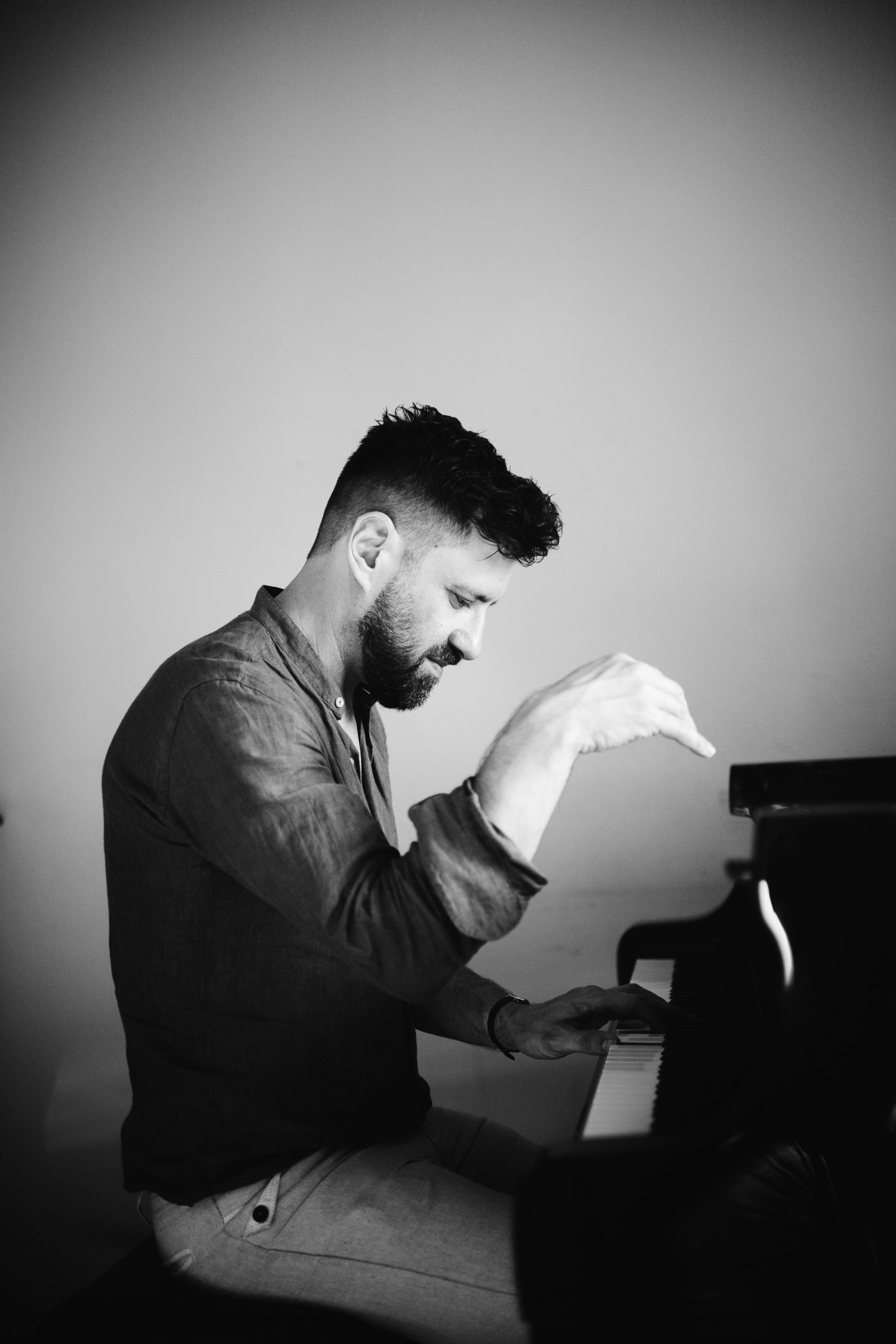 Black and white photo of a bearded man playing piano, captured in a dramatic side profile pose.
