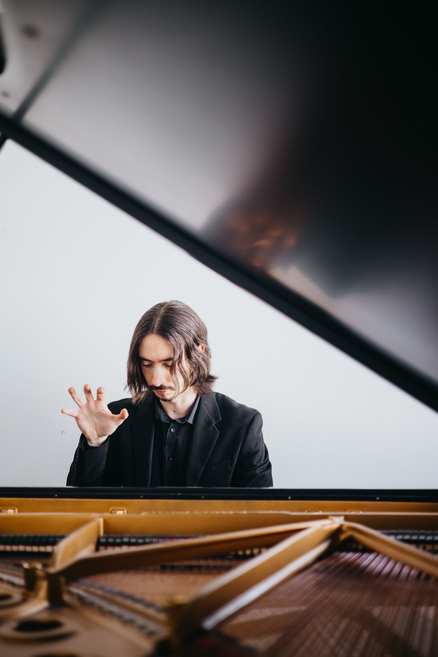 Male pianist with long hair performing expressively at open grand piano.