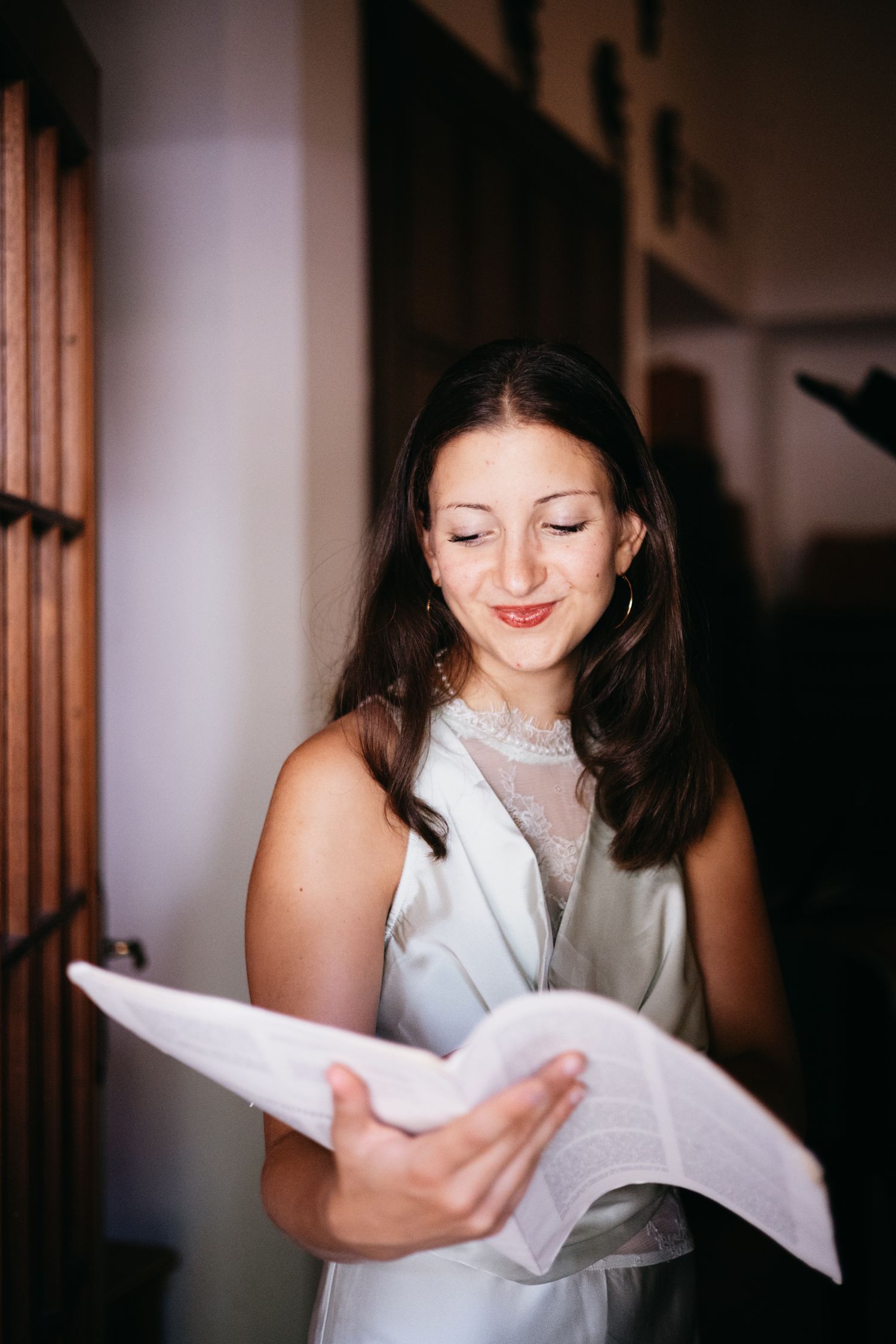 Young woman in silver dress smiling while reading papers indoors.