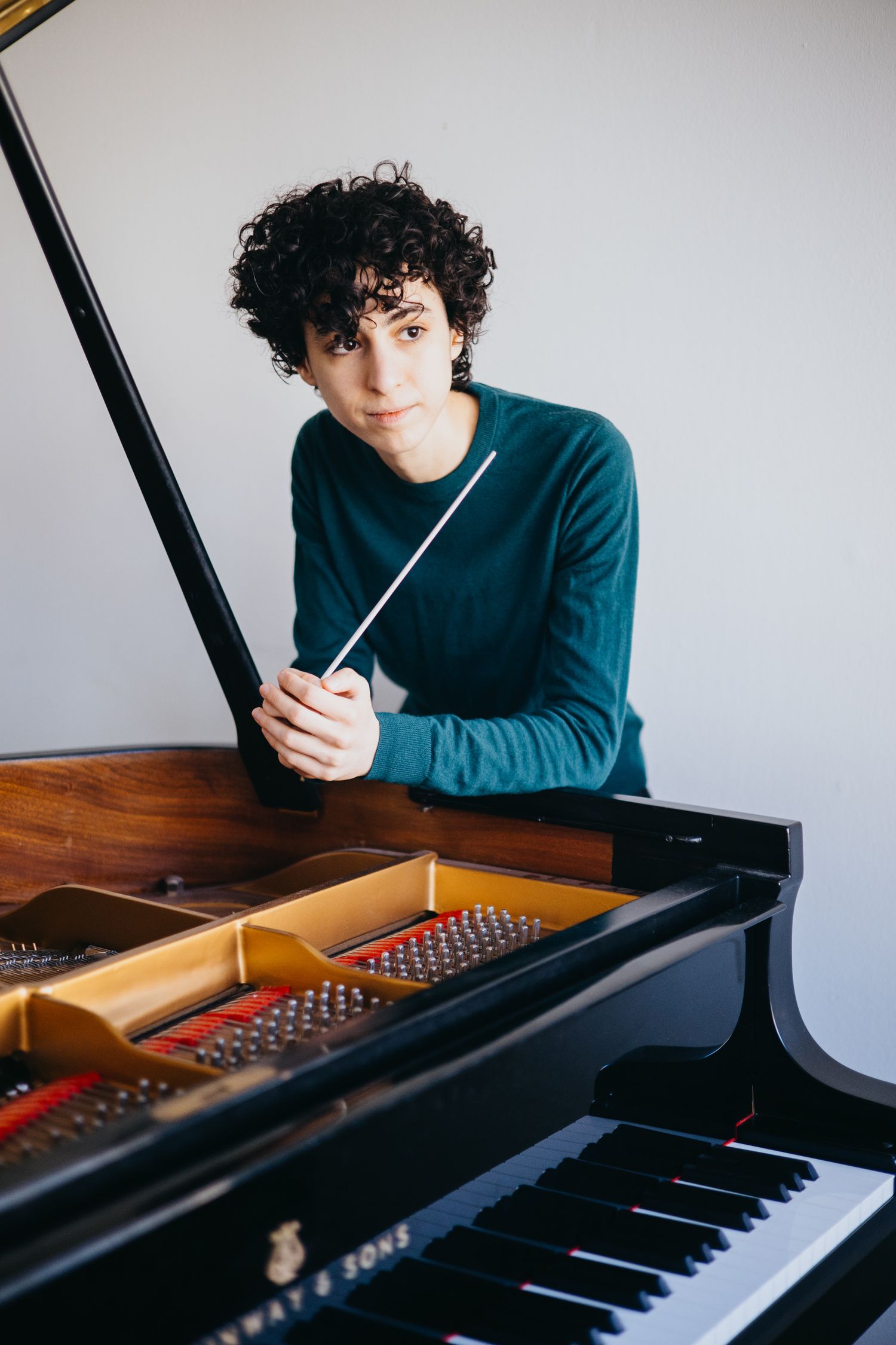 Young conductor holding baton while leaning on a grand piano.