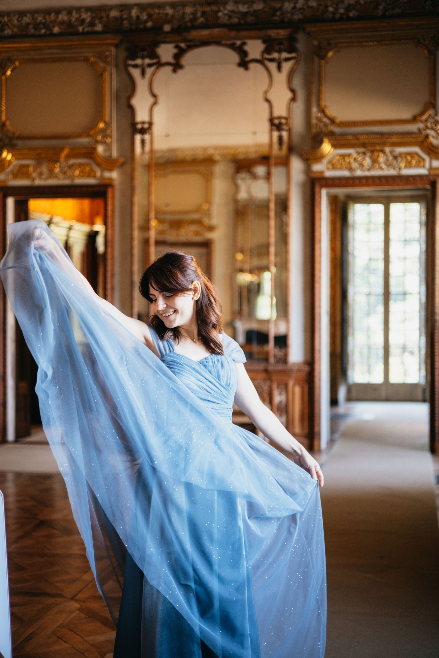 Woman in flowing blue gown twirling in ornate golden ballroom.