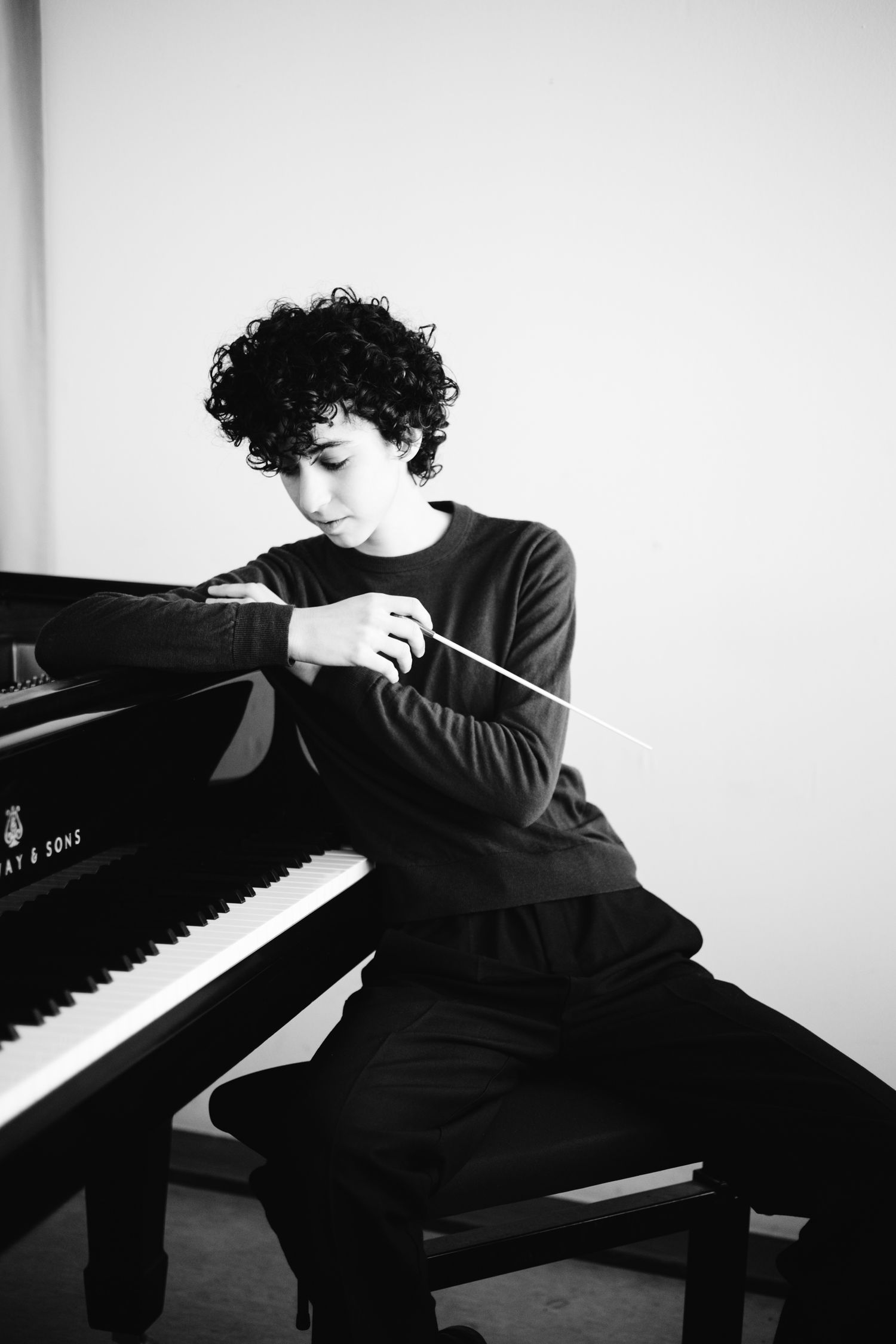 Black and white image of young conductor with baton at grand piano.