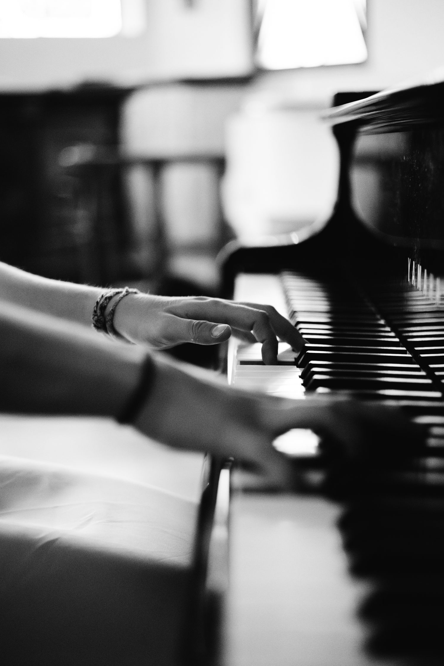 Black and white photo of hands playing a grand piano, wearing bracelets, captured in elegant close-up.