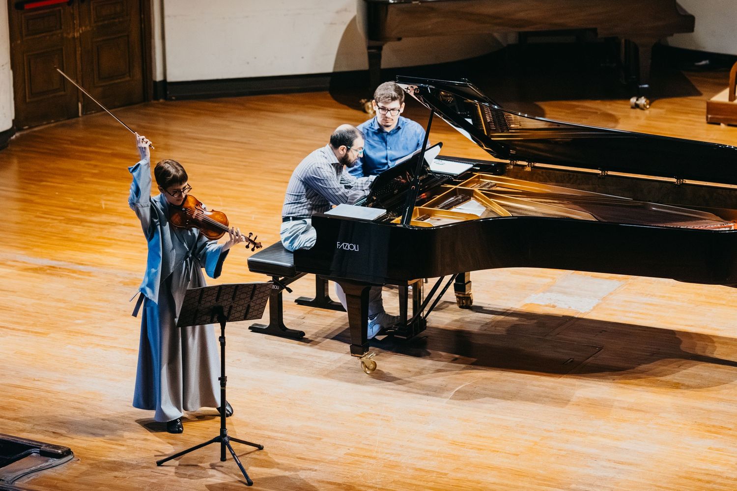 Two musicians perform together at grand piano on warmly lit concert hall stage.