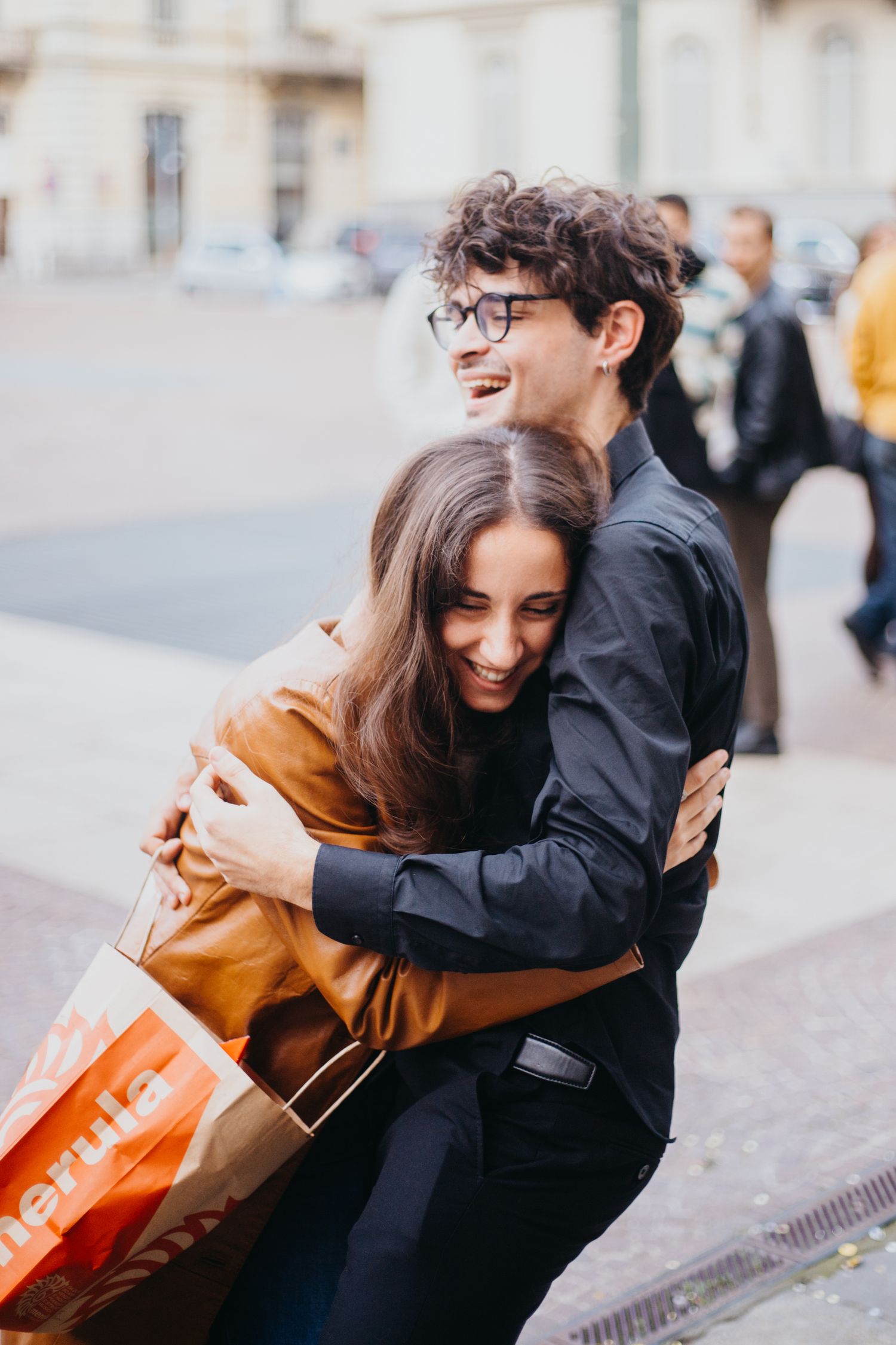 Happy young couple hugging and laughing on a city street during a graduation celebration outdoors.