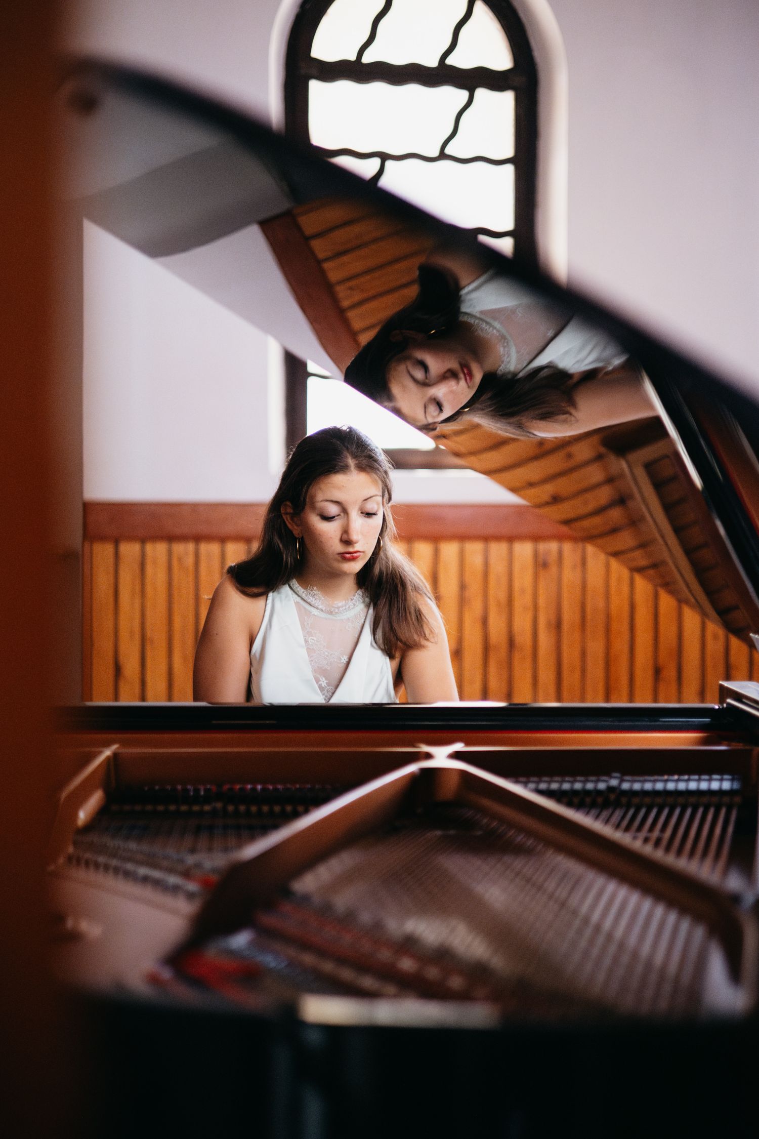 Young woman playing a grand piano viewed from inside the instrument, with a person leaning over the lid above.