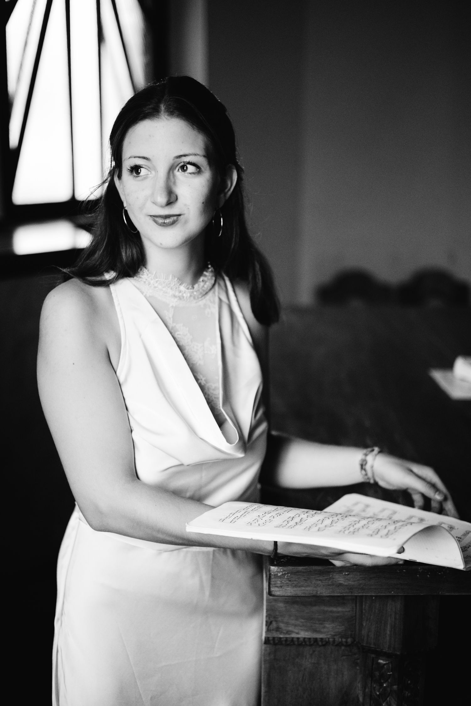 Black and white portrait of a brunette woman in elegant dress holding an open book, posing gracefully indoors.
