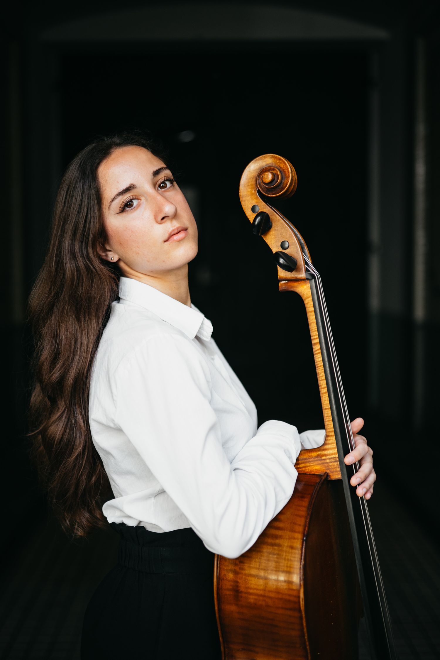 La violoncellista Cecilia Caminiti in camicia bianca e sfondo scuro fotografata da Marco Carino, fotografo specializzato in musicisti