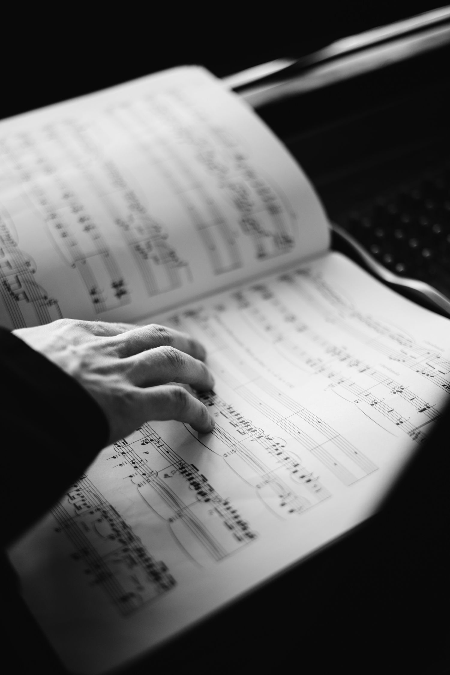 Black and white close-up of hands on sheet music at grand piano keyboard.