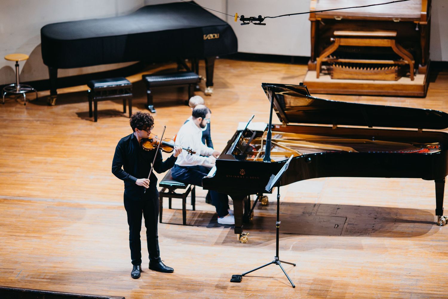Violinist performs on stage with pianist accompanist in a concert hall during a music recital.