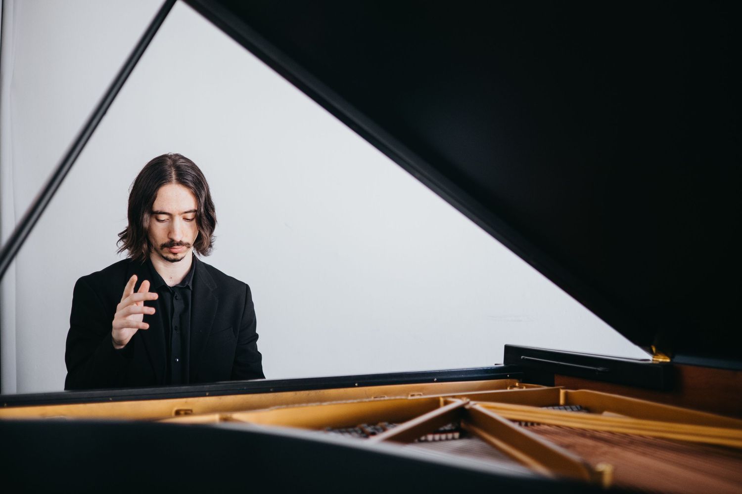 Male pianist in black suit seated at grand piano, gesturing expressively during a performance.