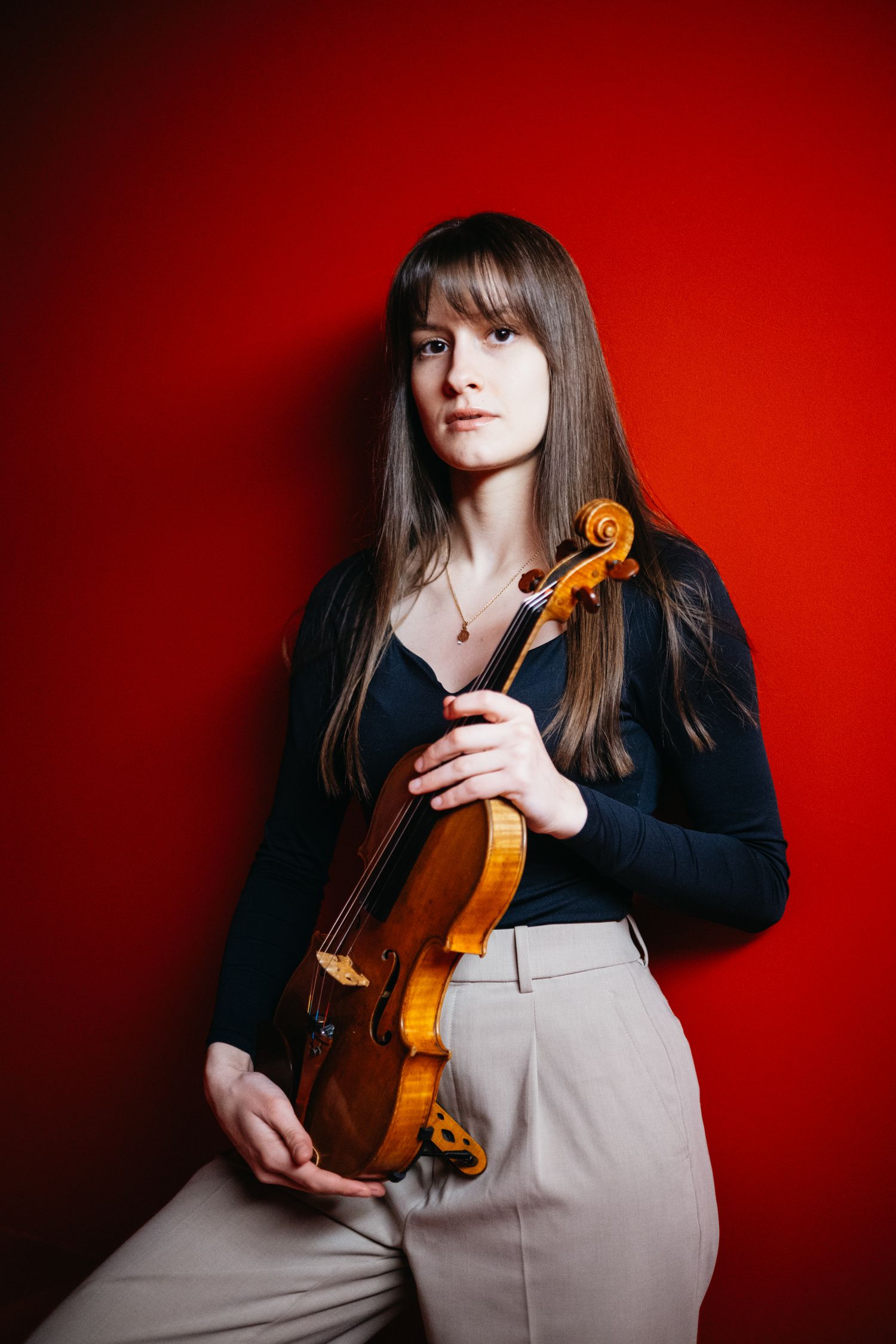Female violinist in black top holding a violin against a vibrant red background.