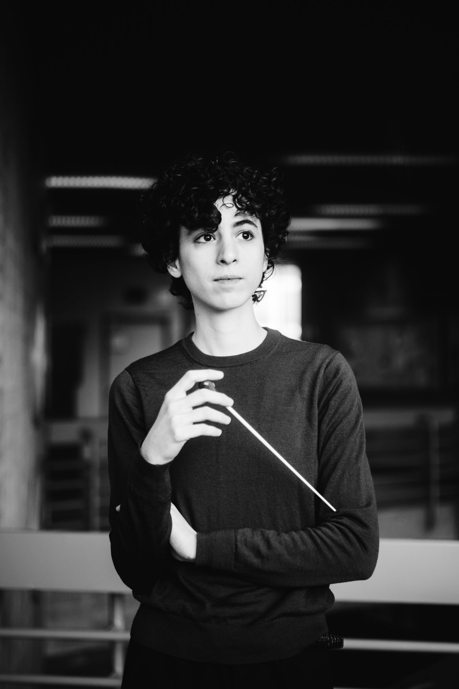 Black and white portrait of young conductor holding baton indoors.