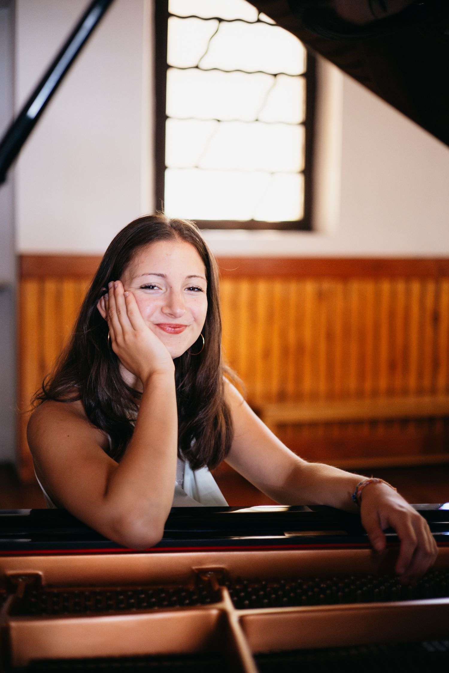 Young woman smiling warmly while leaning on a grand piano in a bright music room.